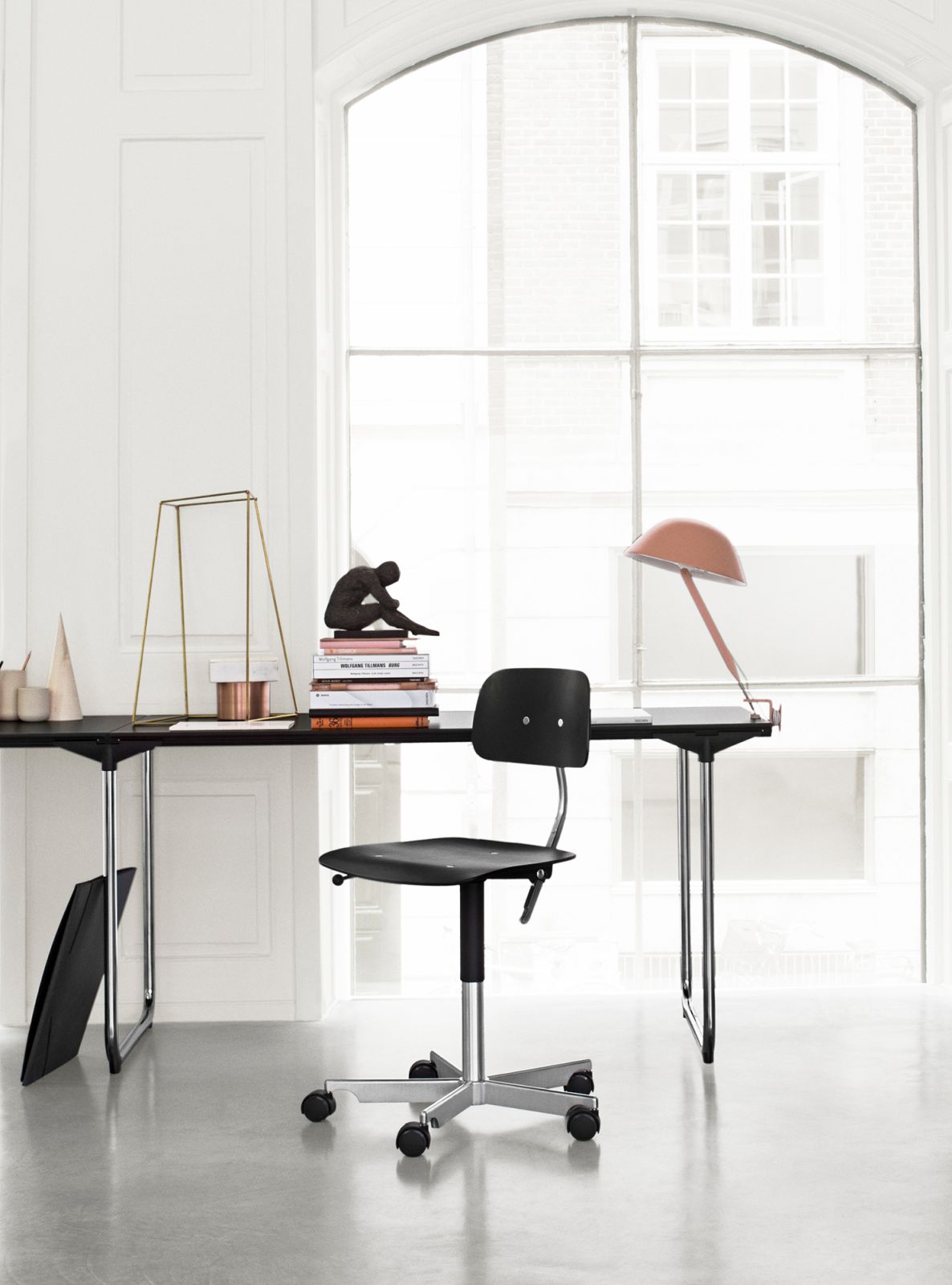 Schwarzer Kevi Bürostuhl mit Rollen vor einem Schreibtisch, ideal für modernes Homeoffice und Büro.