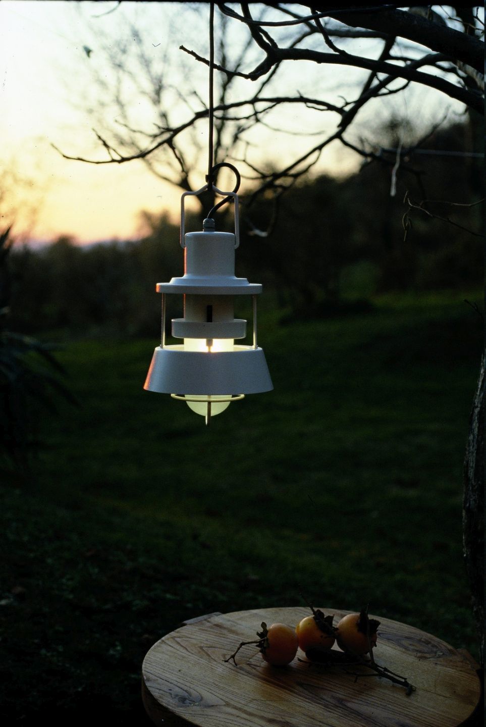 Martinelli Luce Polo Outdoor Pendelleuchte, weiße Hängelampe im Garten mit warmem Lichtschein über einem Holztisch.