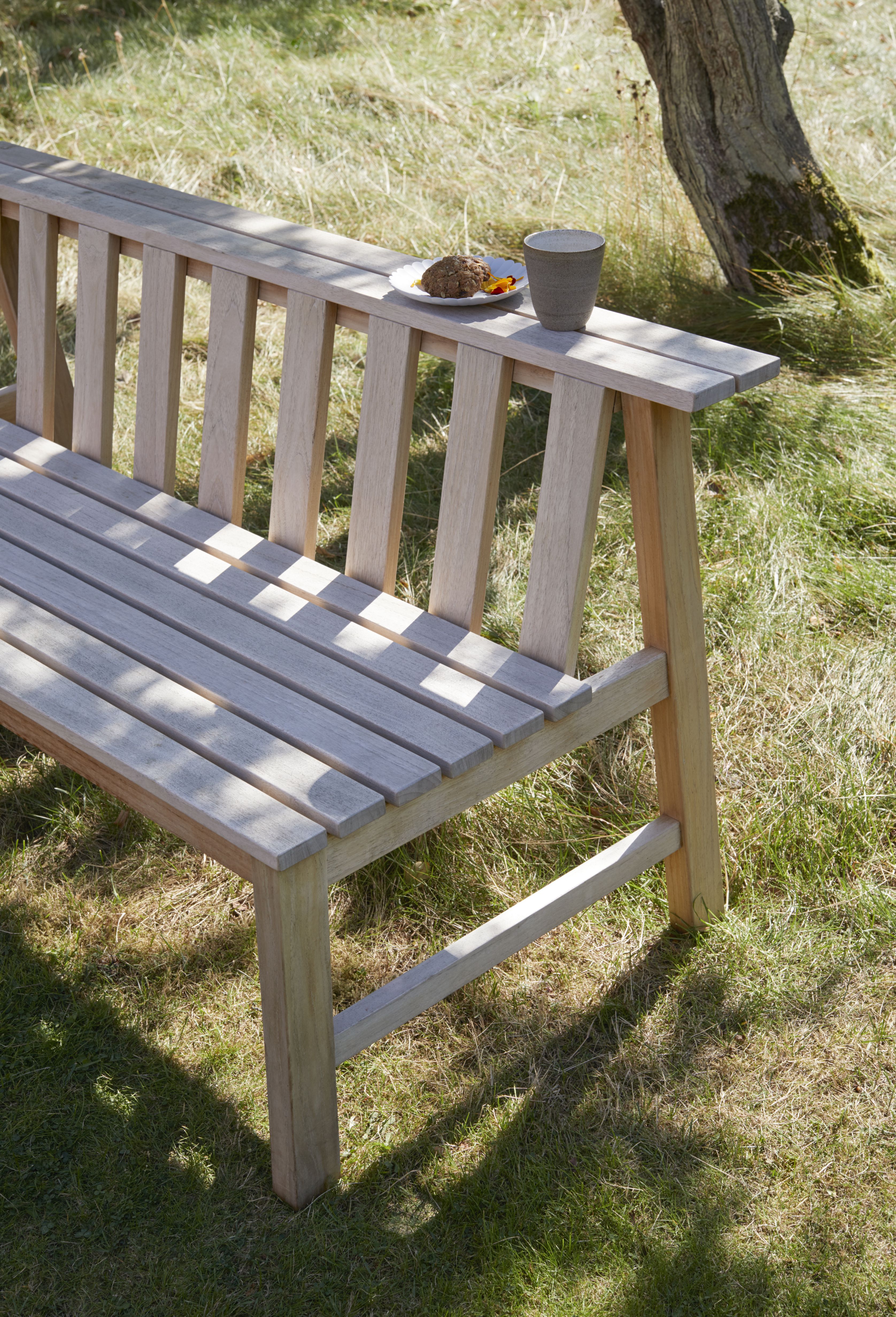 Cadence Bank Teak Gartenbank von Skagerak by Fritz Hansen im Außenbereich mit Tasse und Gebäck.