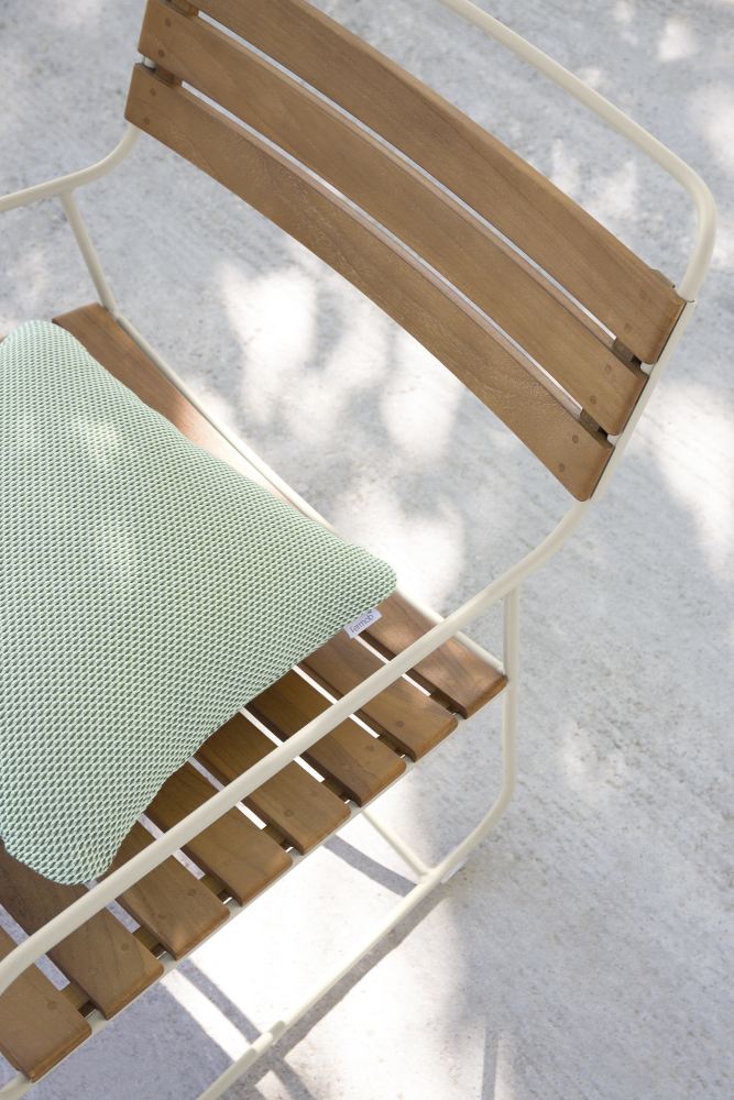 Detailaufnahme des Fermob Surprising Teak Chair Outdoor Stuhls mit grünem Kissen, Teakholz und weißem Metallgestell.