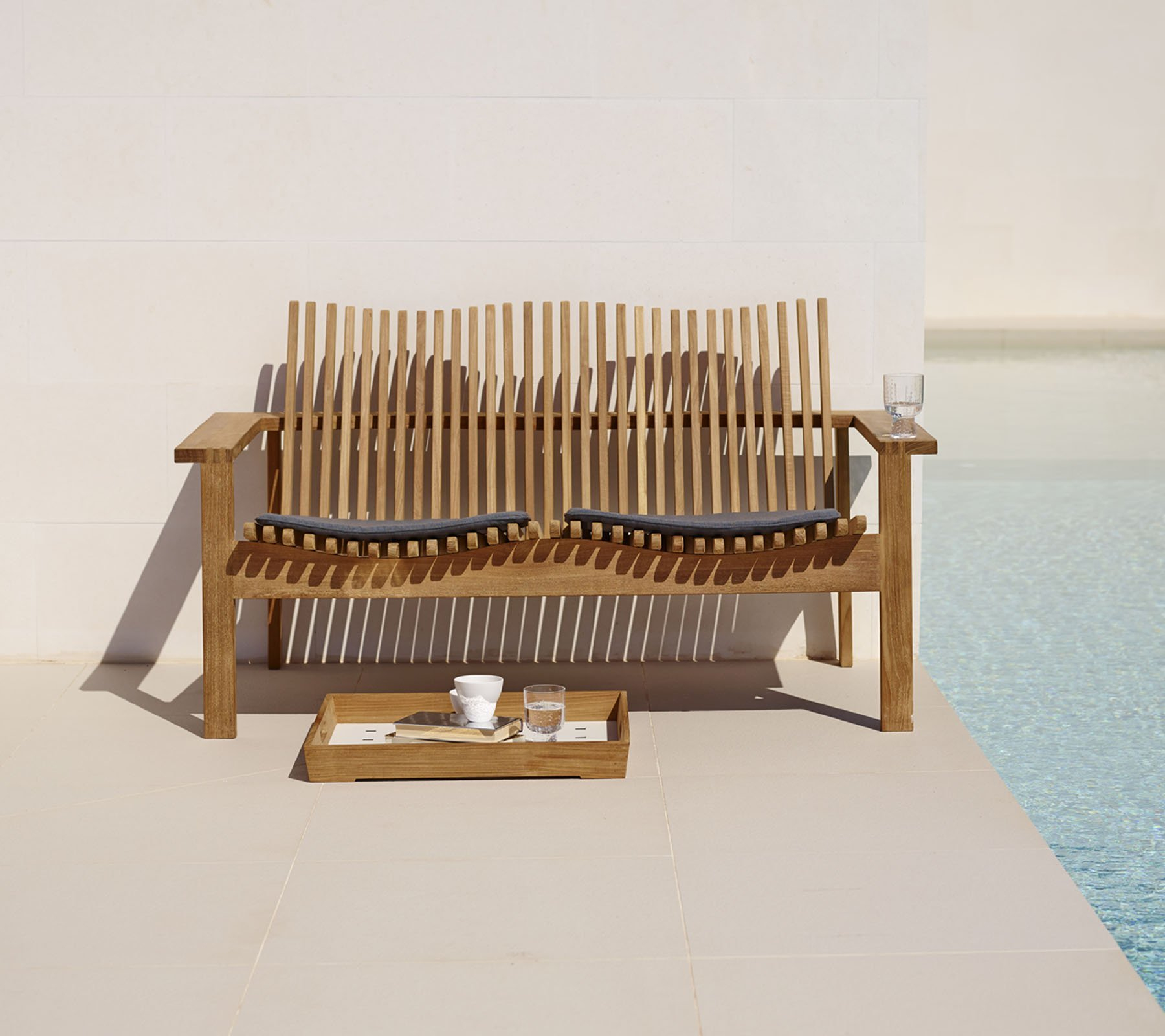Amaze Cane-Line 2-Sitzer Gartensofa aus Teakholz mit grauen Kissen und Getränken.
