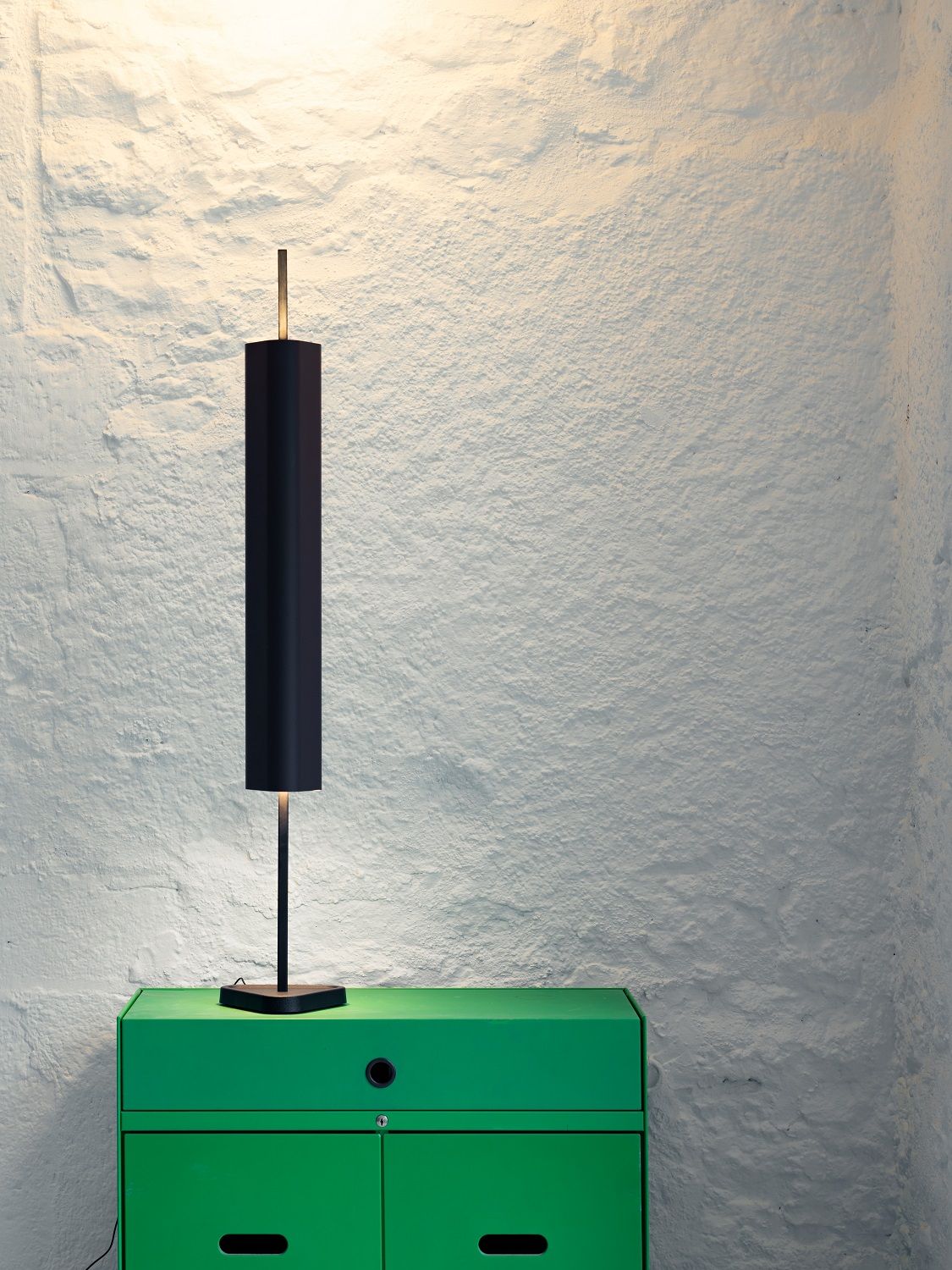 Schwarze Emi Table Tischleuchte von Flos auf einem grünen Schrank vor einer weißen Wand.