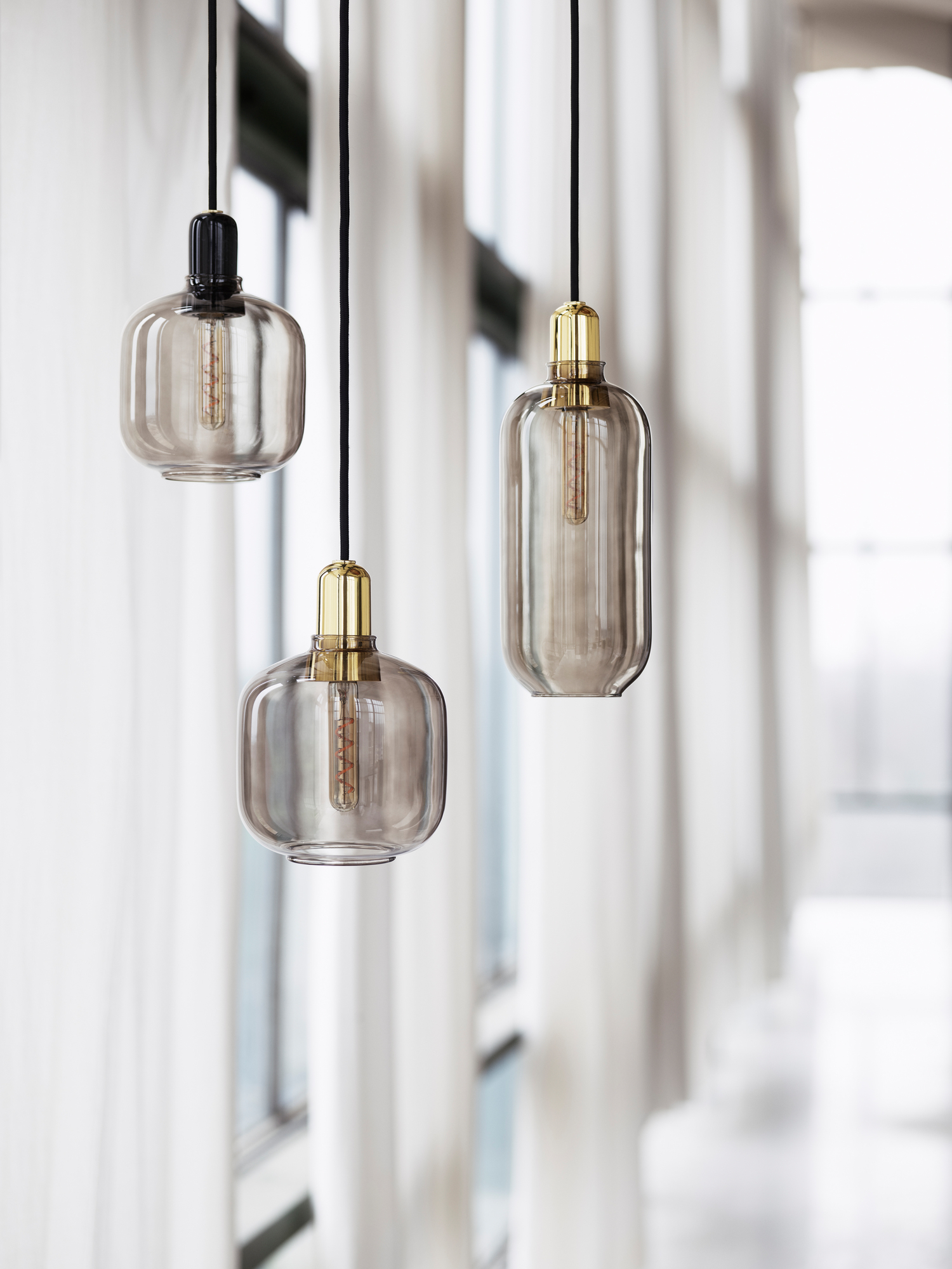 Drei moderne Amp Lamp Pendelleuchten von Normann Copenhagen in Gold und Grün vor hellem Hintergrund.