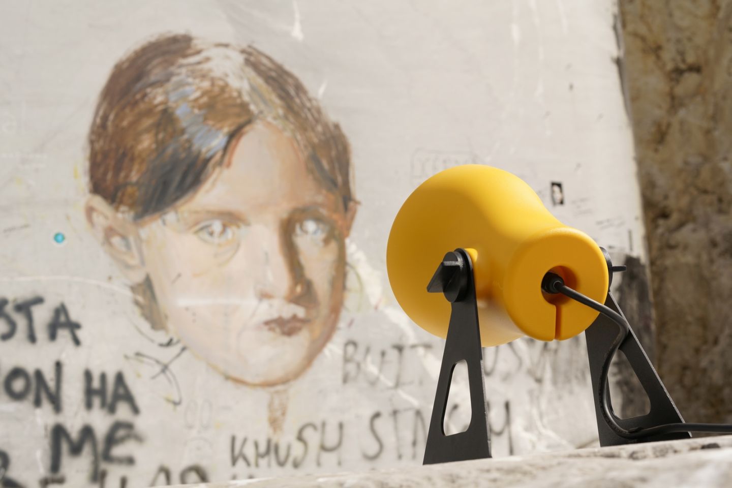 Gelbe Martinelli Luce Mini Frog Outdoor Leuchte vor einer Wand mit Graffiti und einem Kinderportrait.