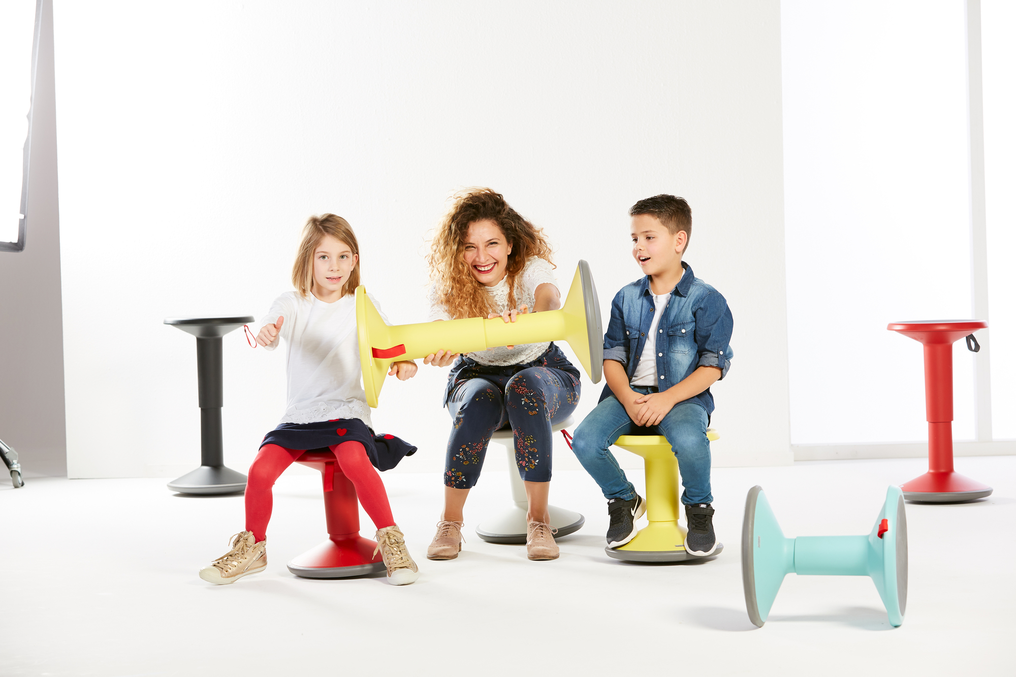 Kinder und Frau sitzen auf UP Junior Edition Kinderhocker Interstuhl, lachsorange, ergonomische Sitzmöbel für Kinder.