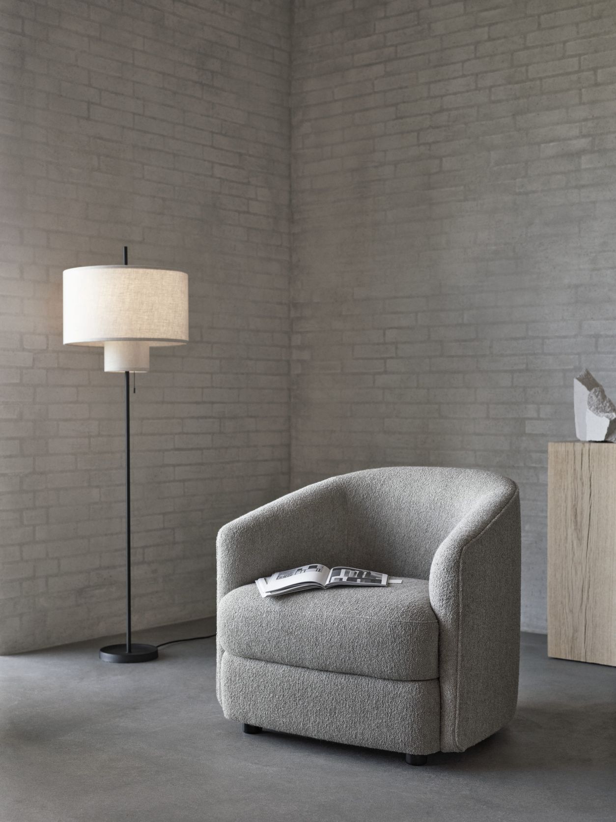 New Works Margin Stehleuchte neben grauem Sessel in modernem Wohnzimmer mit Backsteinwand.