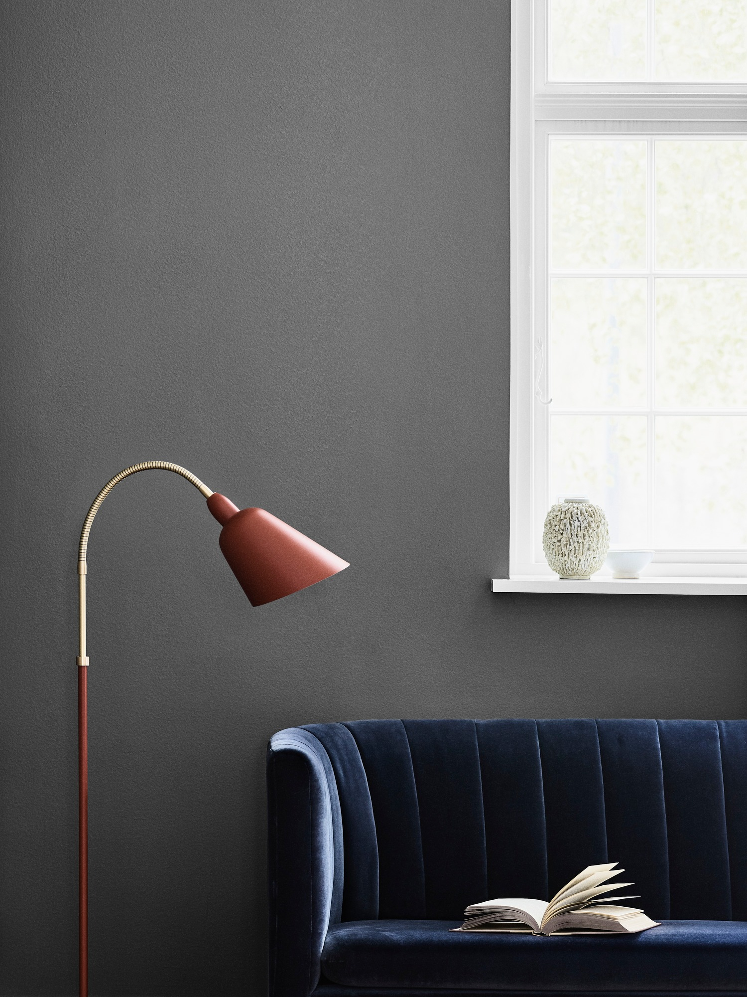 AndTradition Loafer Sofa, blaues Samt Sofa mit Buch und roter Stehlampe vor Fenster.