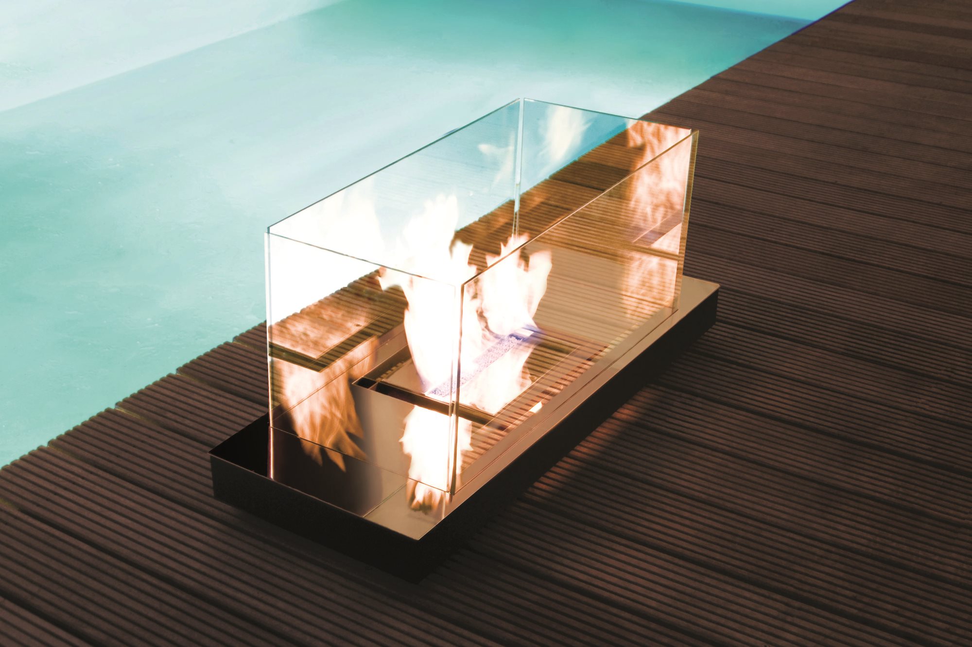 Uni Flame Ethanol Kamin Radius mit Glasumrandung und Flamme auf einer Holzterrasse neben einem Pool.
