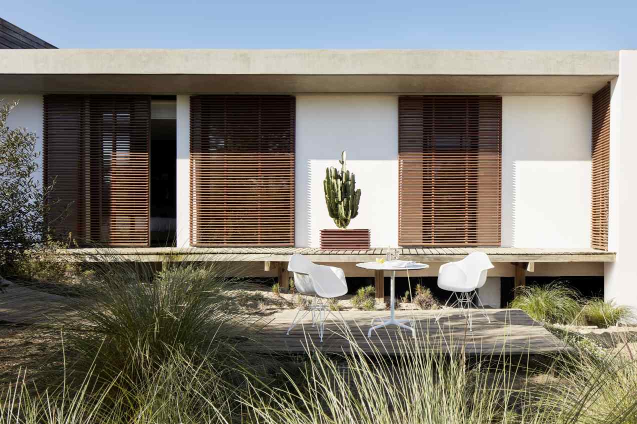 Eames Contract Table von Vitra, runder Tisch mit weißen Stühlen auf einer Holzterrasse vor modernem Haus.