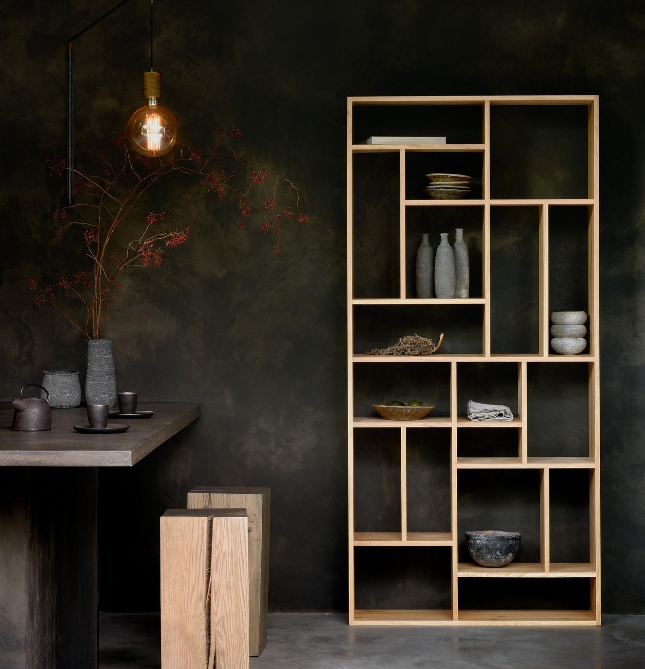 Helles Holzregal mit unregelmäßigen Fächern, dekoriert mit Vasen und Schalen, neben Tisch und Hockern.