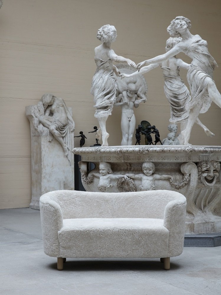 Audo Mingle Sofa, ein cremefarbenes 2-Sitzer Sofa aus Stoff, vor Statuen in einem Museum.