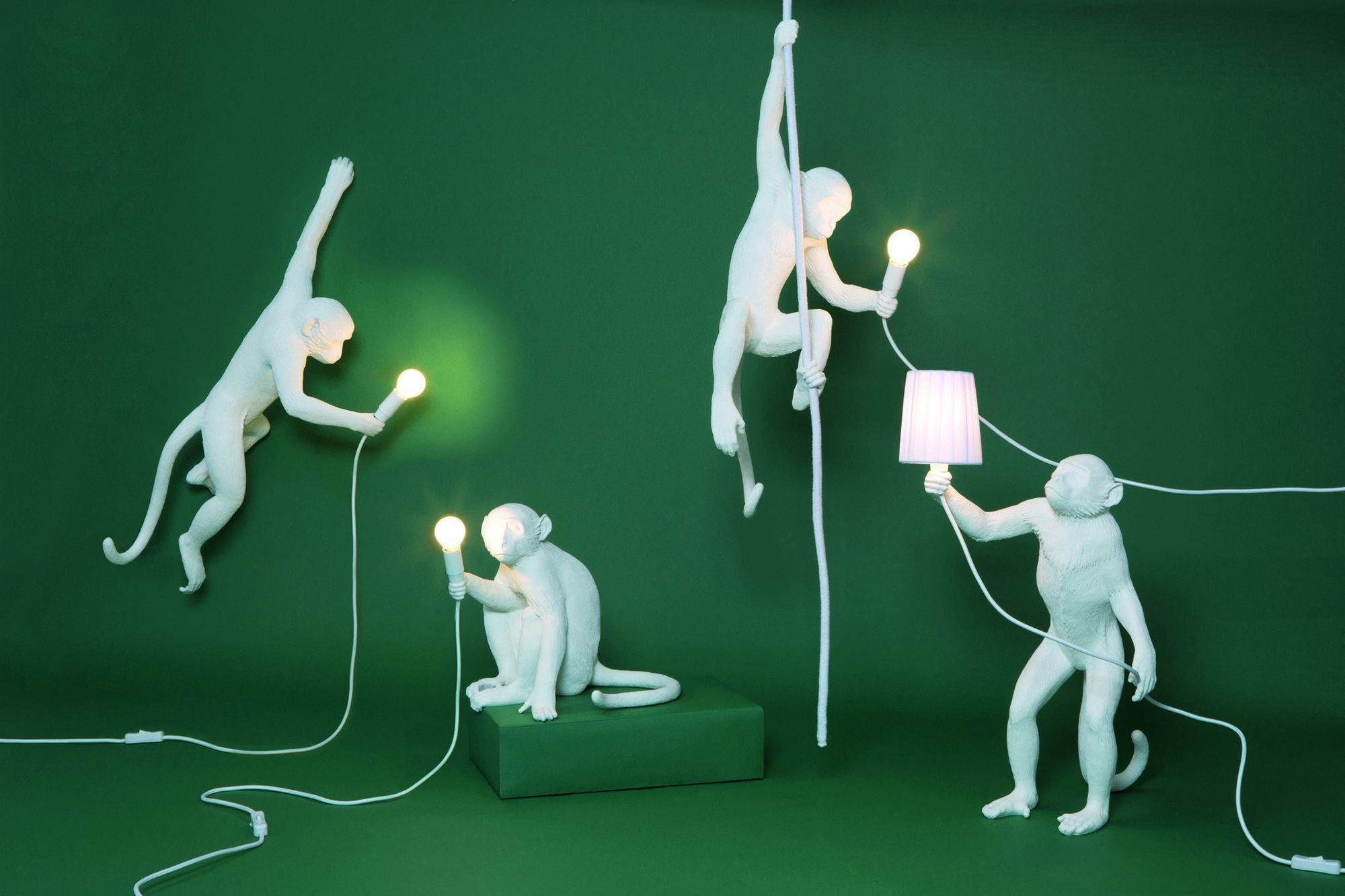 Verspielte Seletti Monkey Lamp Pendelleuchten Indoor, weiße Affenfiguren mit Glühbirnen und Schalter vor grünem Hintergrund.