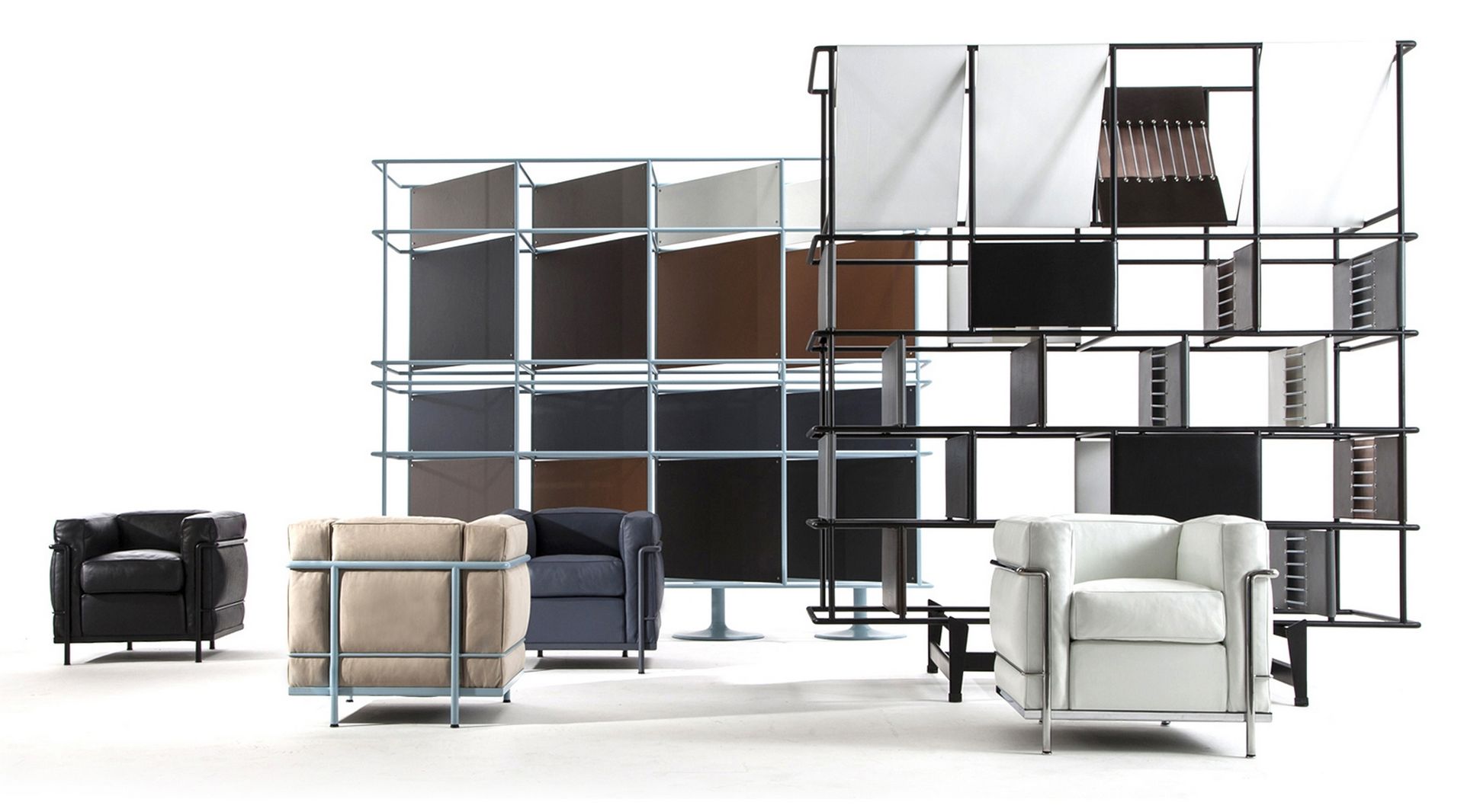 Mehrere Cassina Grand Confort Sessel in Schwarz, Beige, Blau und Weiß vor modularen Regalsystemen.