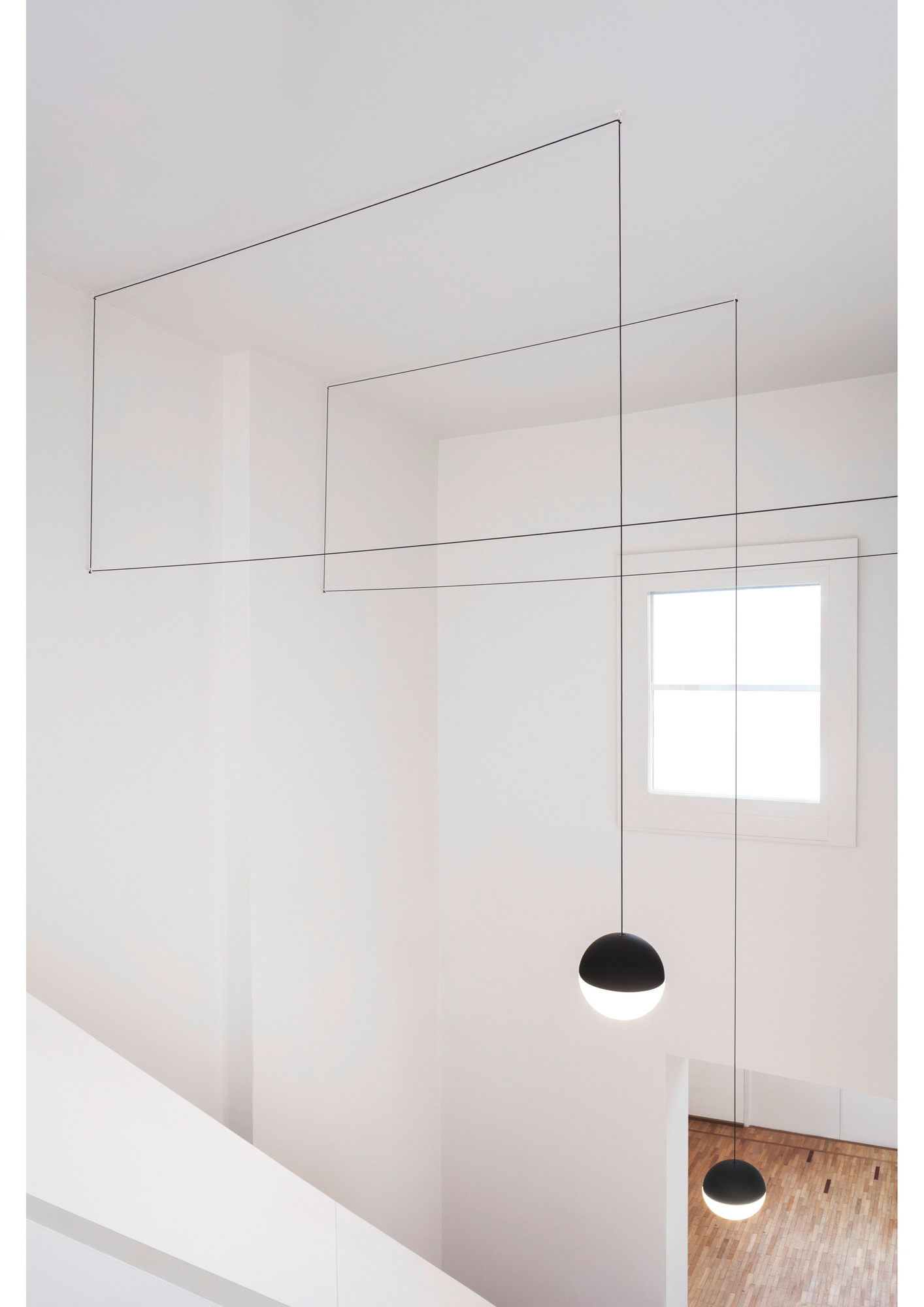 Zwei schwarze String Light Kugelkopf Pendelleuchten von Flos hängen in einem Treppenhaus.