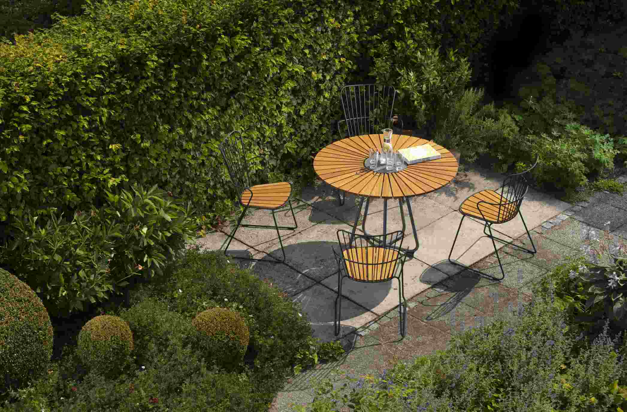 Houe Circle Gartentisch Ø 110 cm mit vier Stühlen auf einer Terrasse im Grünen.