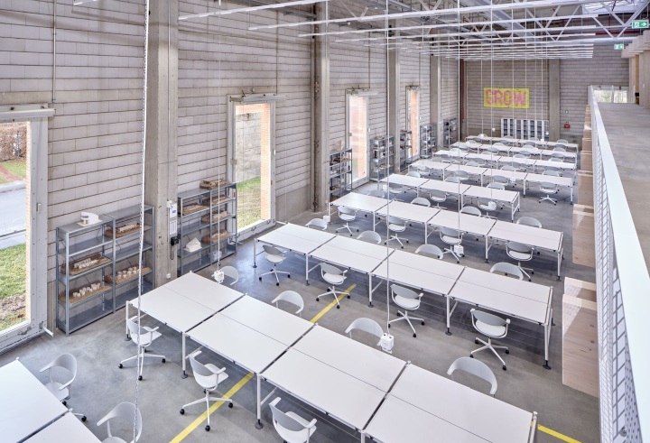 Helle Werkshalle mit Reihen von weißen Tischen und Mynt Bürodrehstühlen von Vitra, modernes Design.