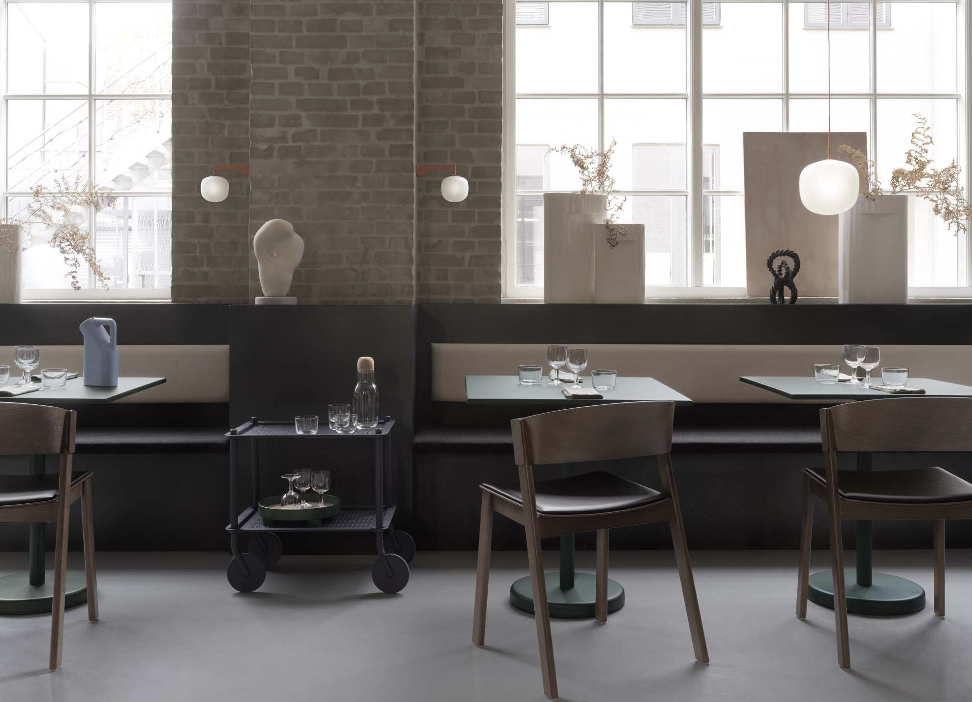 Innenaufnahme eines Restaurants mit dem Muuto Flow Trolley Servierwagen, Tischen, Stühlen und dekorativen Elementen in modernem Design.