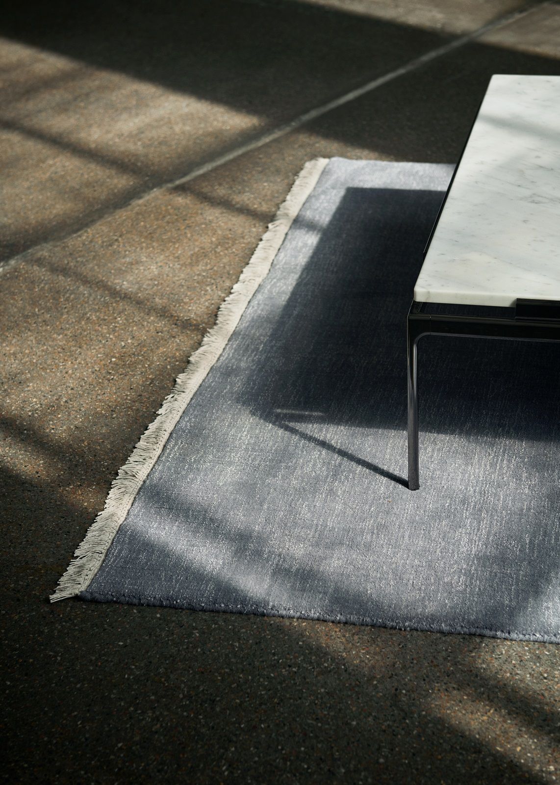 Detailaufnahme des grauen AndTradition Teppichs "The Moor AP19 Rug" mit Fransen und einem Tischbein.