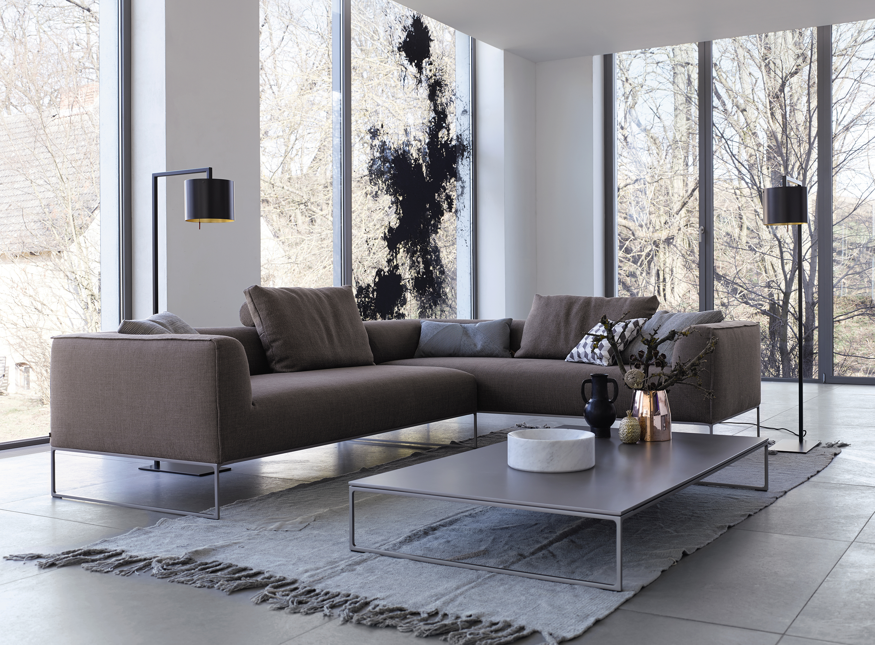 Mell Lounge Sofa in Braun mit Kissen und Couchtisch vor großen Fenstern.