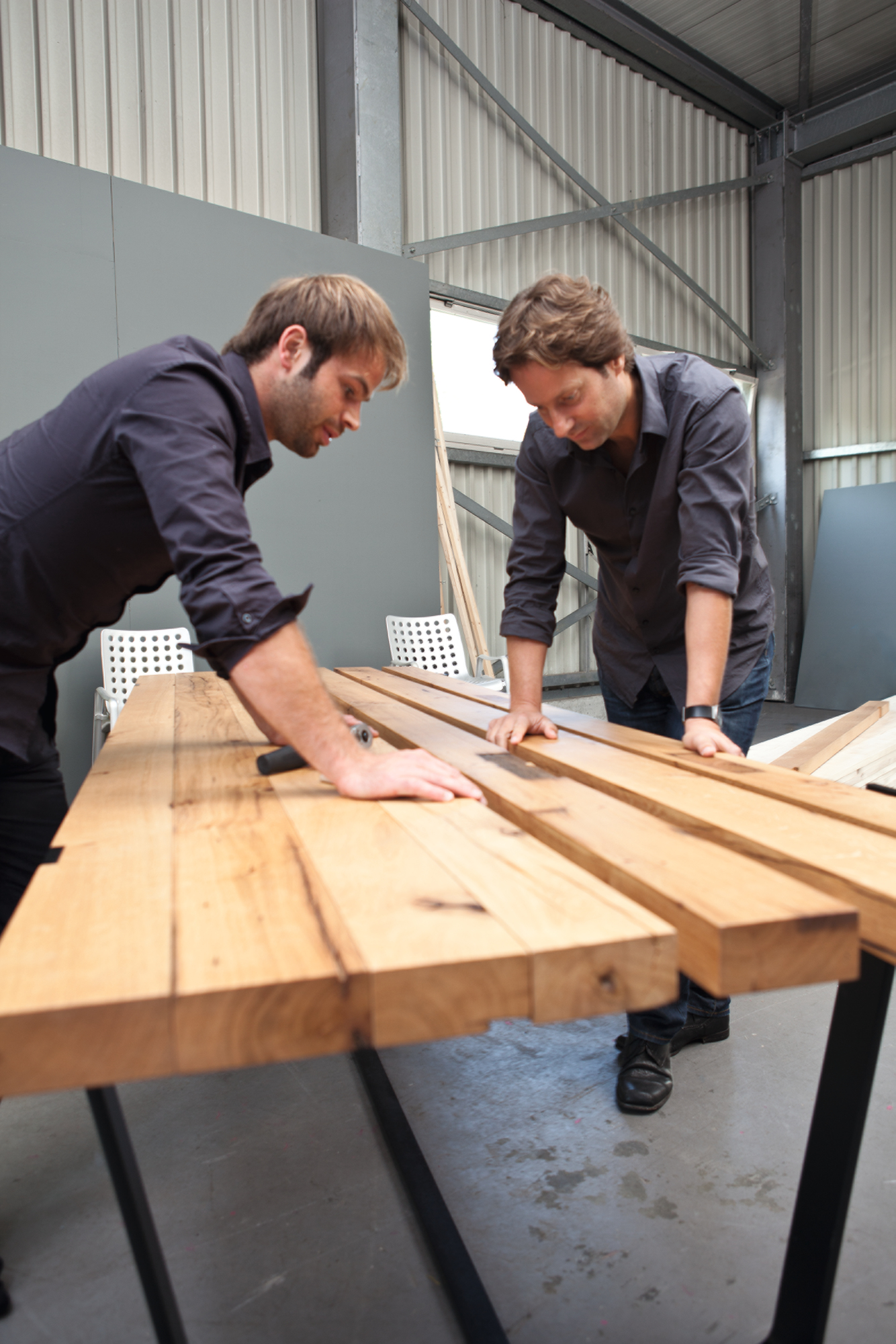 Zwei Männer montieren einen Janua BB 11 Clamp Tisch aus massivem Nussbaumholz in einer Werkstatt.
