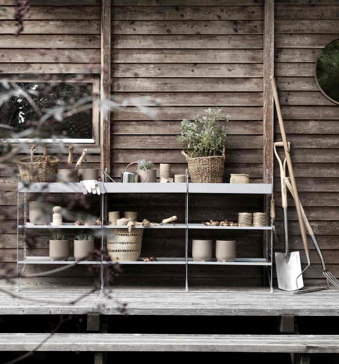String Outdoor Regalsystem mit Gartenzubehör vor einer Holzwand, ideal für Balkon und Terrasse.