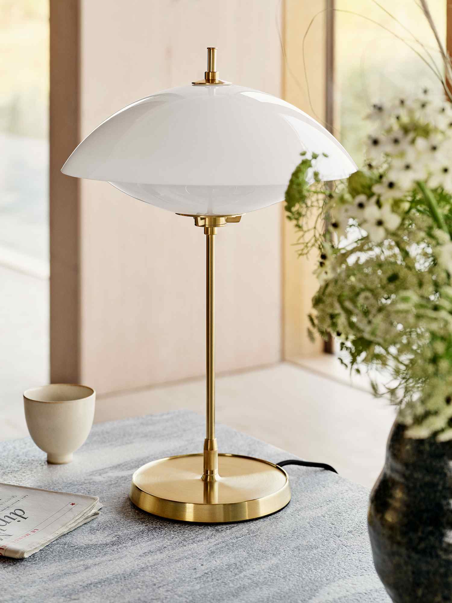 Nahaufnahme der Fritz Hansen Clam Tischleuchte mit weißem Schirm und goldenem Fuß.
