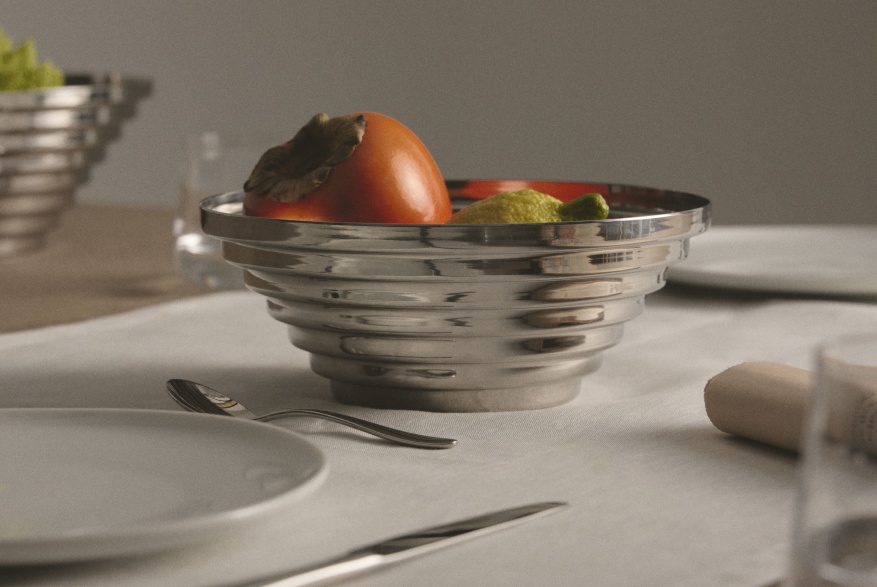 Alessi Maya Schale rund, Ø 20 cm, gefüllt mit Obst, auf gedecktem Tisch. Dekorative Edelstahlschale.