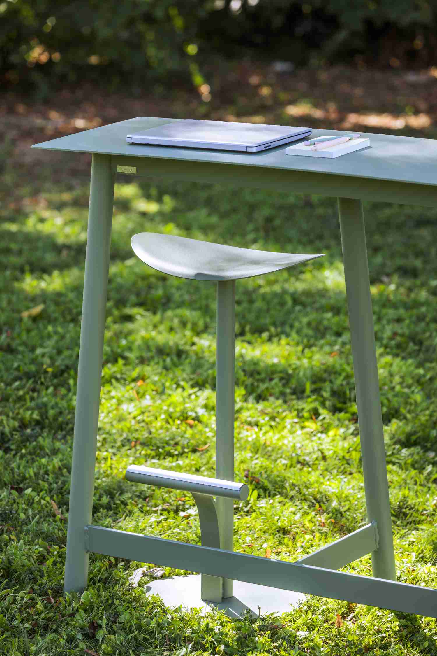 Bolder Barhocker von Fermob im Freien auf Rasen. Moderner, grüner Outdoor-Hocker mit Fußstütze.