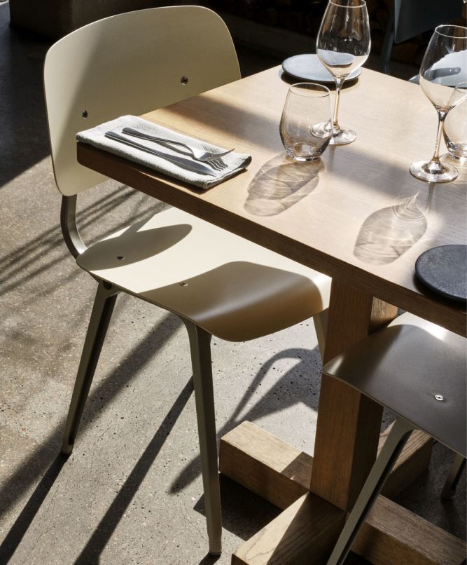 Nahaufnahme eines beigen Revolt Chair Stuhls von Hay an einem Holztisch mit Gläsern und Besteck.