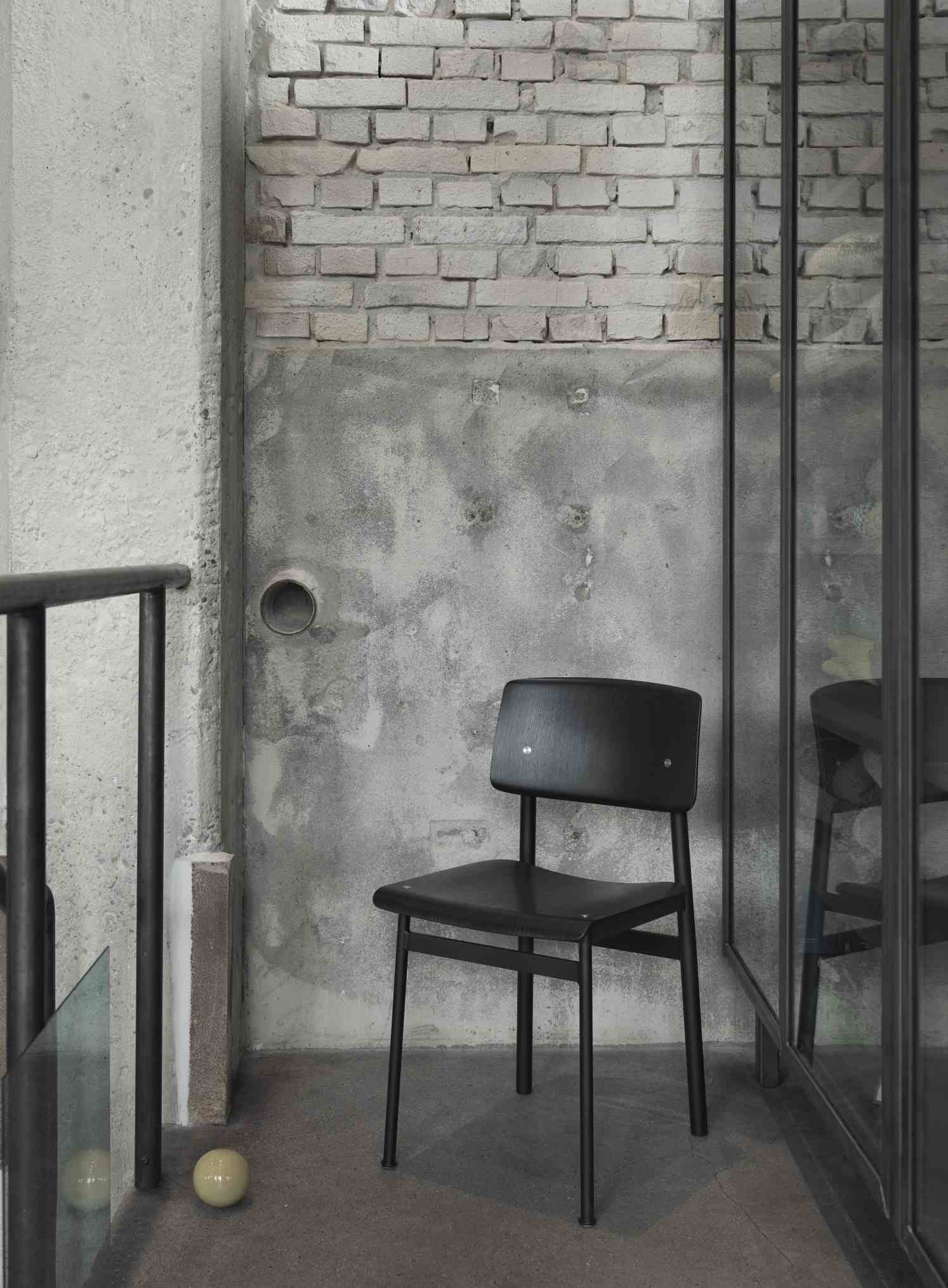 Schwarzer Loft Chair Stuhl von Muuto vor einer Wand mit Ziegel- und Betonstruktur.