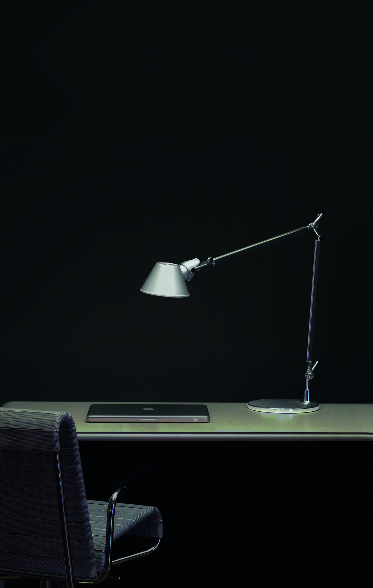 Silberne Artemide Tolomeo Tischleuchte auf Schreibtisch mit Laptop und Bürostuhl vor dunklem Hintergrund.