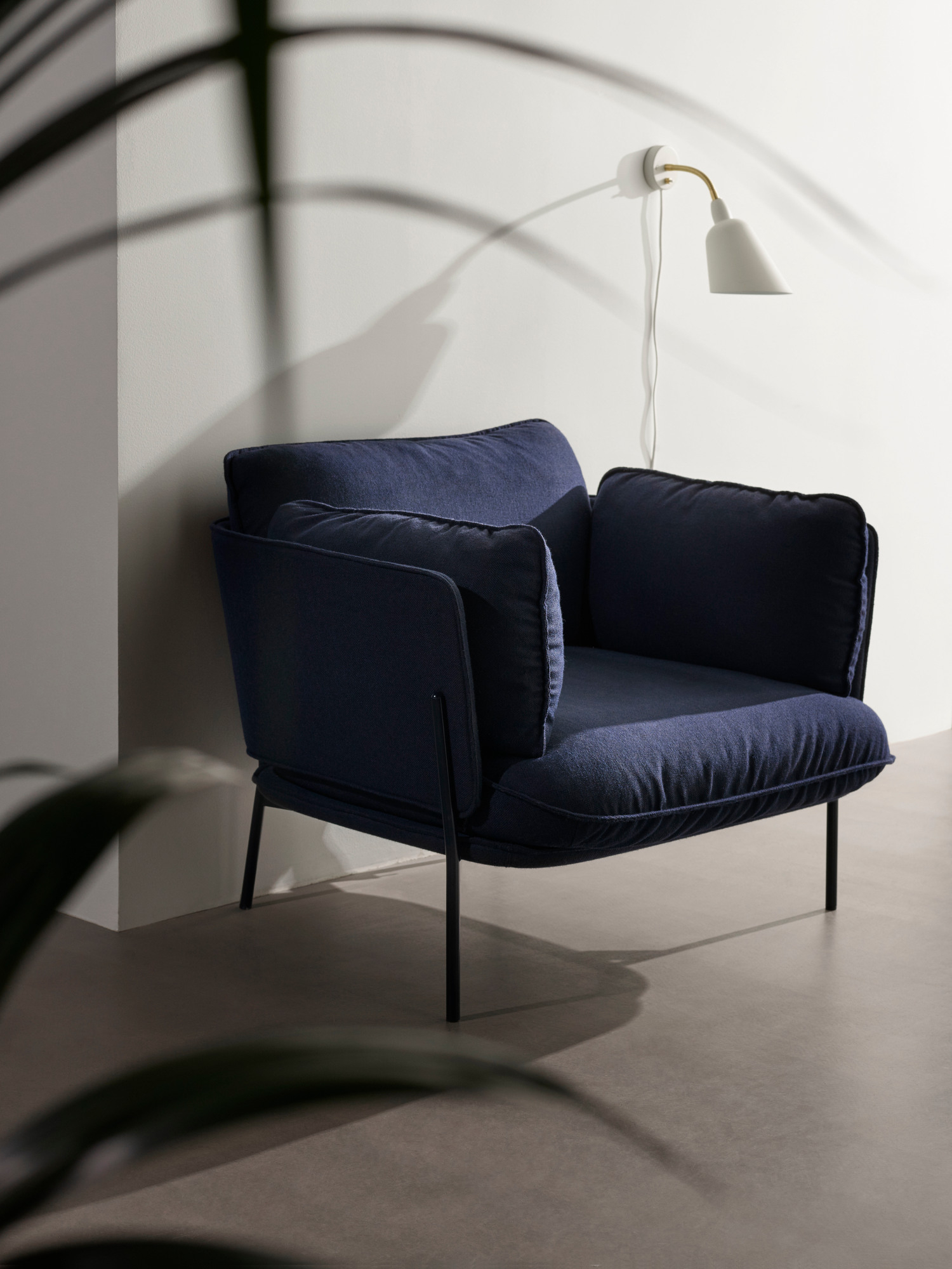 AndTradition Cloud Sessel LN1 in Dunkelblau mit Stahlgestell und passenden Kissen vor einer Wand.