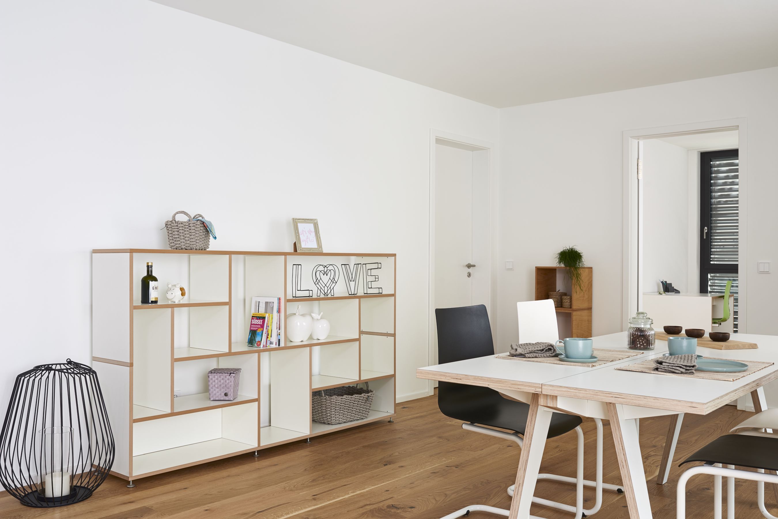 Helles Esszimmer mit modernem Esstisch, Stühlen und weißem Regal mit Deko-Elementen.