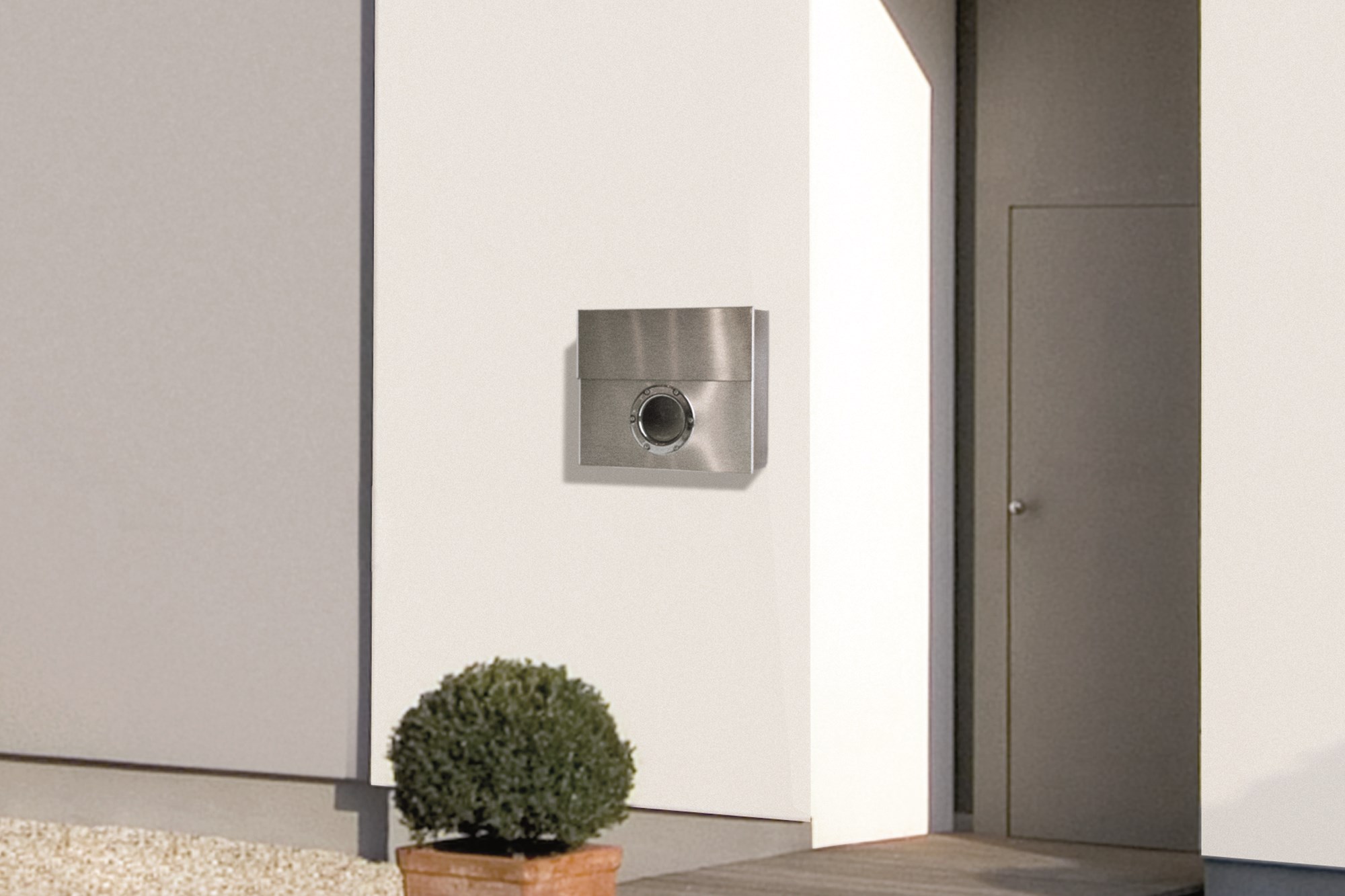 Moderner Edelstahl Briefkasten mit Kamera und Gegensprechanlage an weißer Hauswand, Pflanze im Vordergrund.