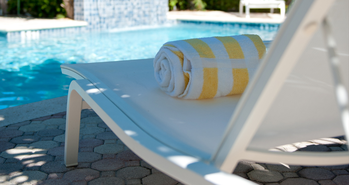 Weiße Alizé Sonnenliege von Fermob am Pool mit gelb-weiß gestreiftem Handtuch, ideal für den Garten.