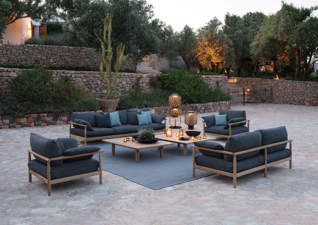 Tibbo Armlehnstuhl von Dedon mit grauer Polsterung und passendem Sofa, Sesseln und Couchtisch im Garten.
