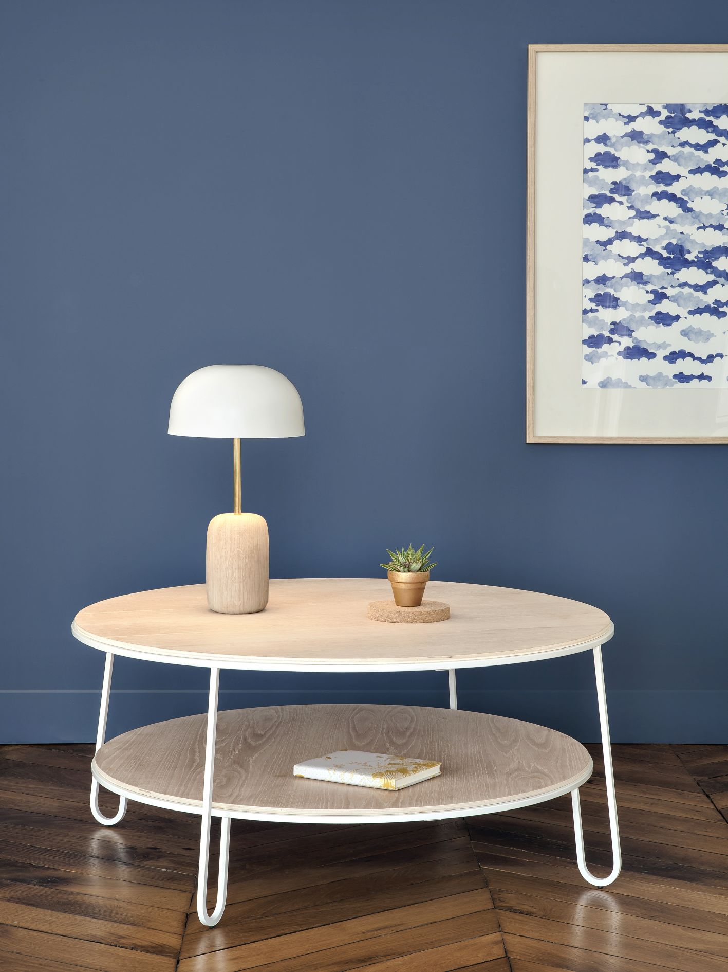 Runder Eugenie Couchtisch von Hartô mit Ablage, Lampe und Pflanze vor blauer Wand.
