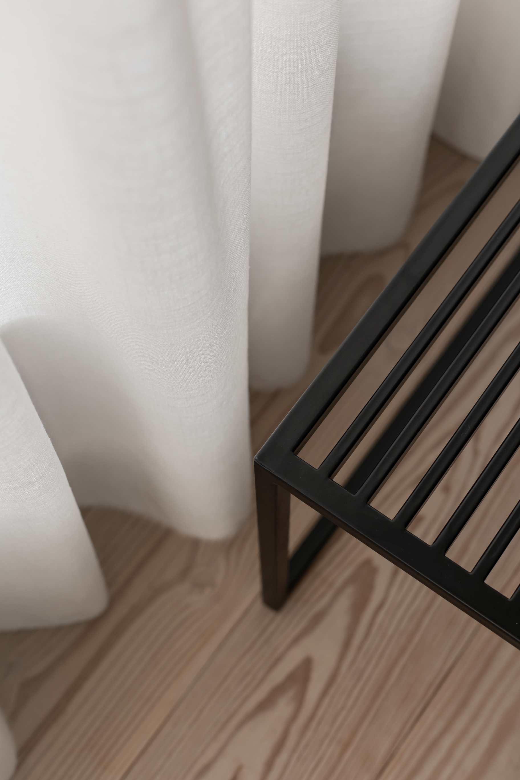 Novoform Element Bank in Schwarz, minimalistisches Design mit Holzfußboden und weißem Vorhang im Hintergrund.