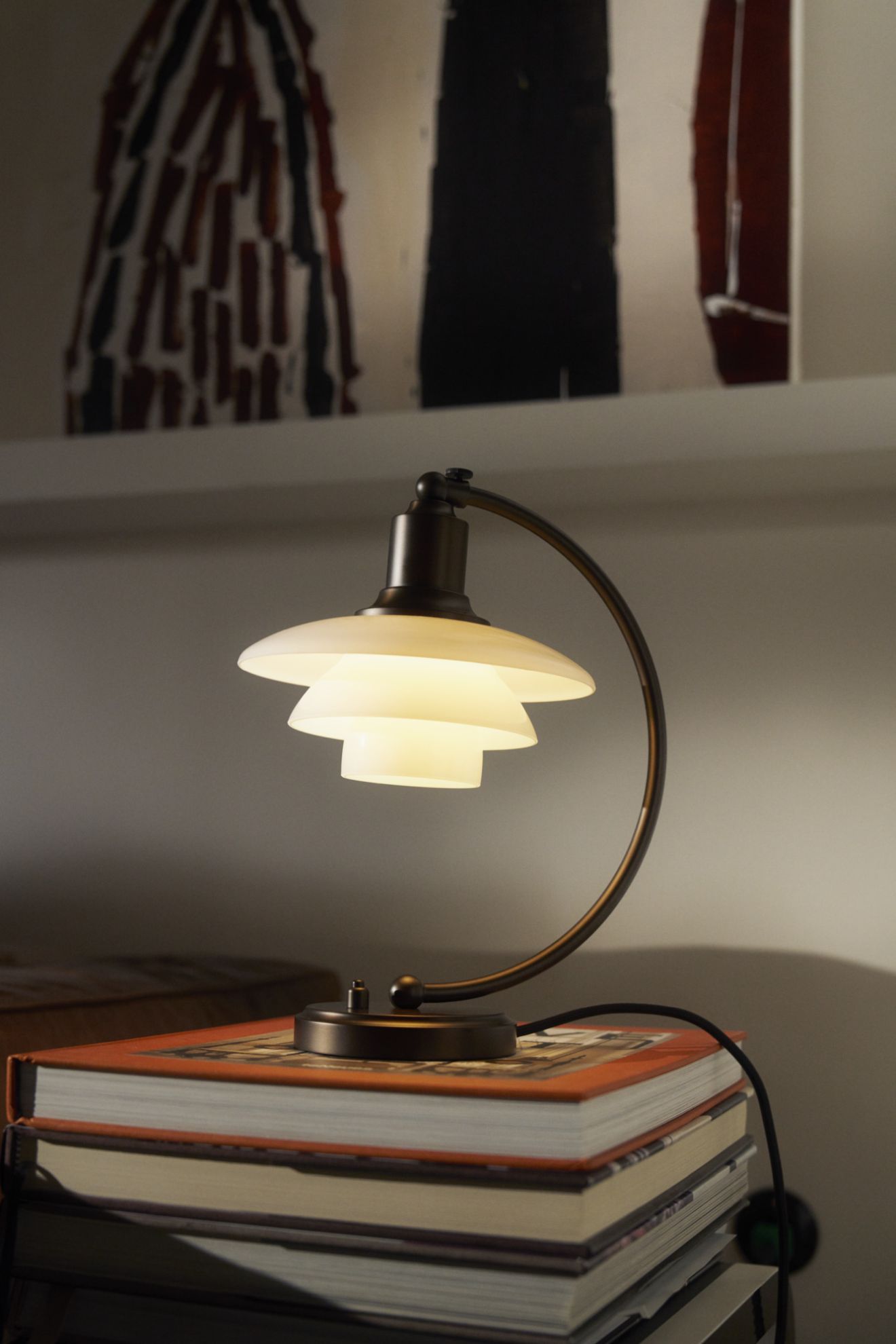 Nahaufnahme der PH 2/2 Luna Tischleuchte von Louis Poulsen in Messing und Opalglas auf Bücherstapel.