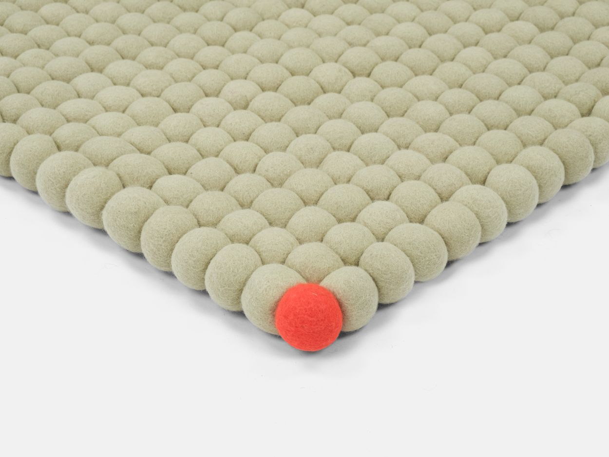 Detailansicht: Grünbeiger Filzteppich "Big One" von myfelt (180x260cm) mit Filzkugeln und einer roten Kugel.