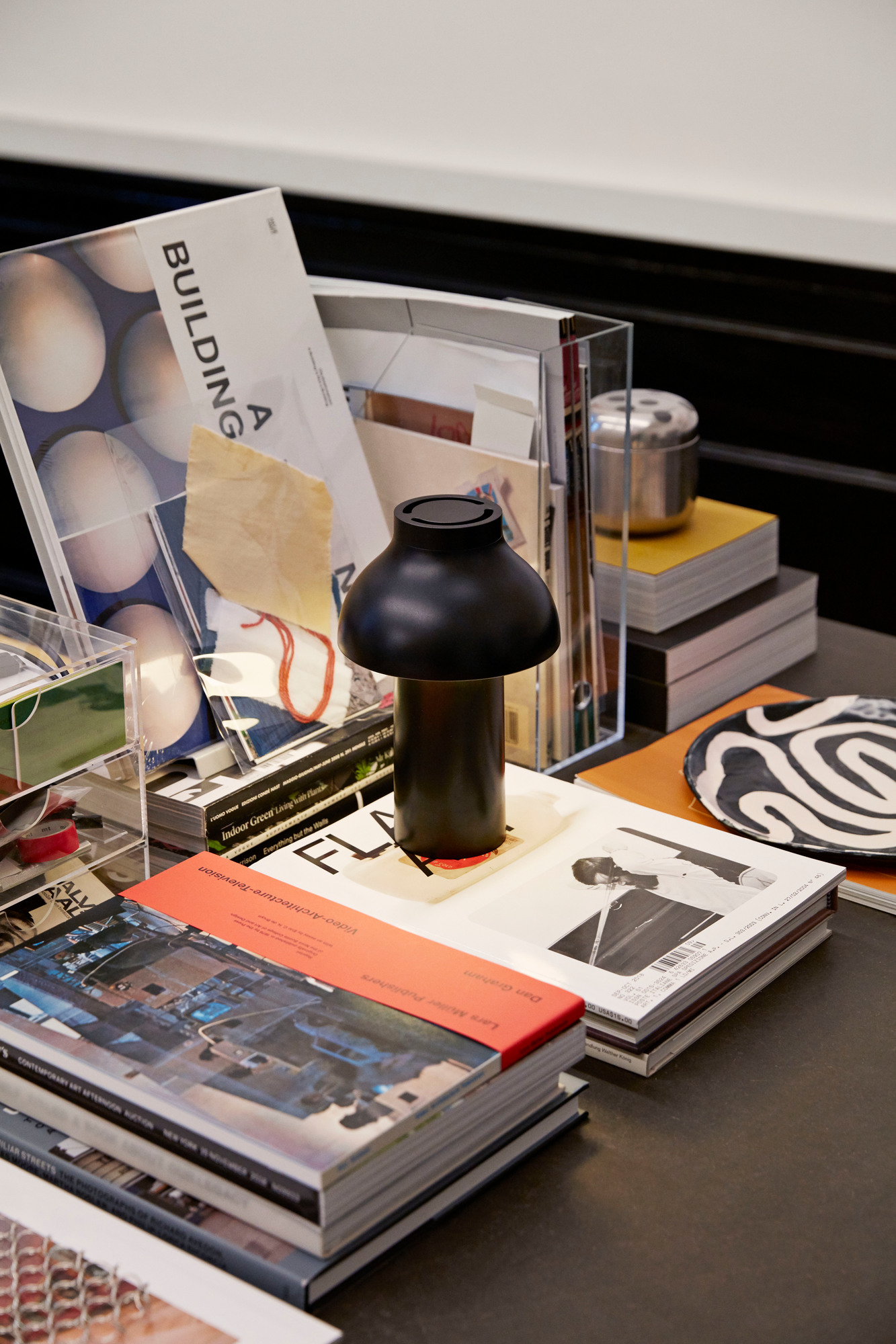 Schwarze Hay PC Portable Akkuleuchte auf einem Stapel Bücher, moderne Tischleuchte für Innenräume.