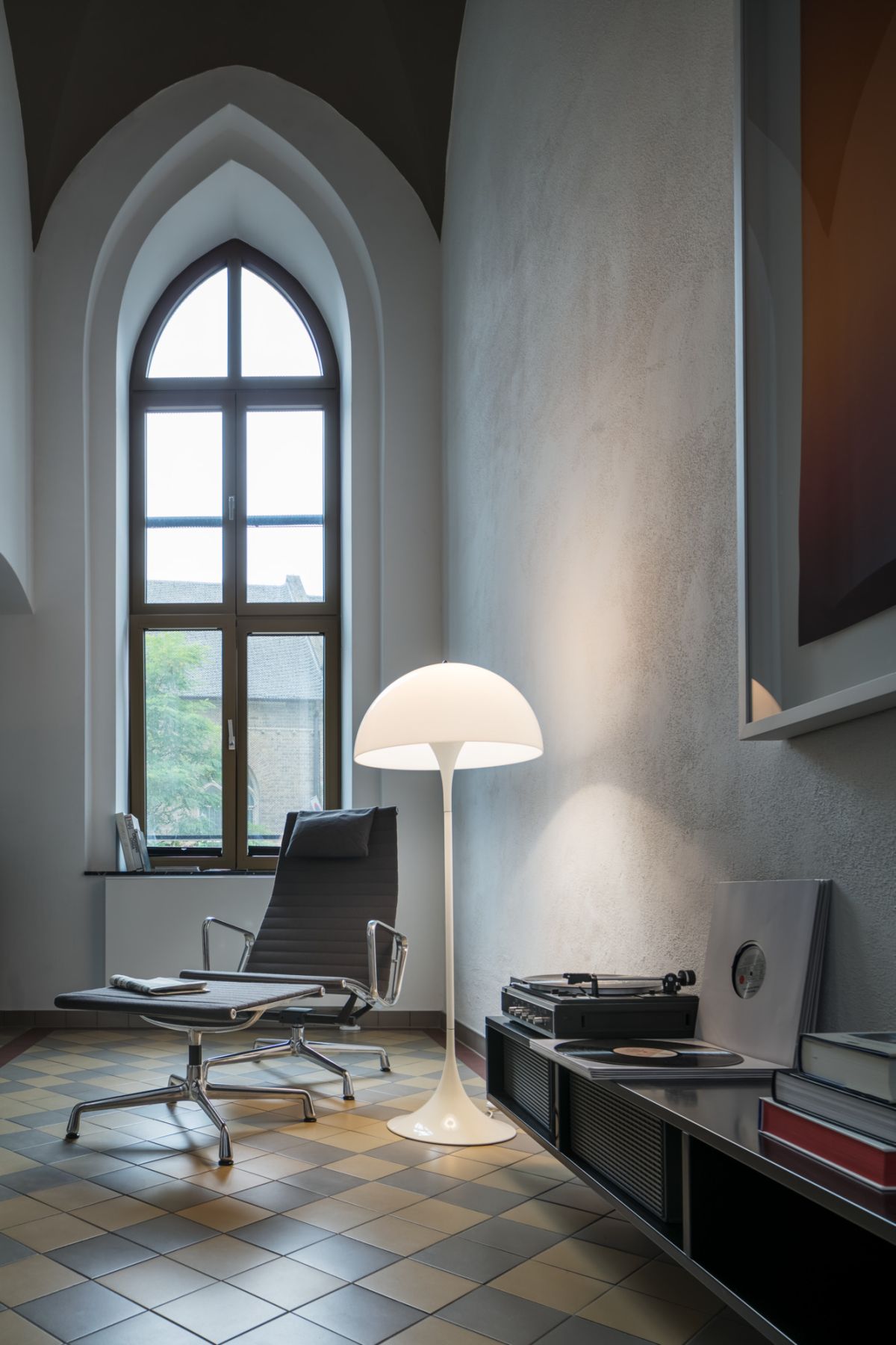 Moderner Lesesessel mit Hocker, Tulip Stehlampe und Schallplattenspieler in stilvollem Wohnzimmer mit großem Fenster.