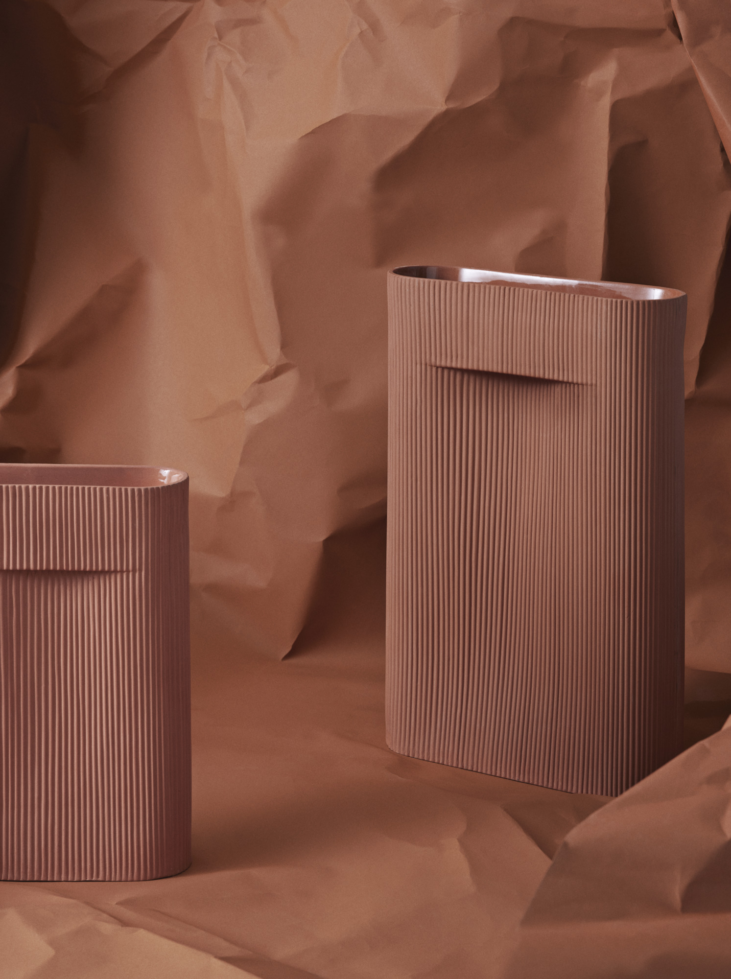 Zwei gerippte, braune Vasen, möglicherweise Ridge Vasen, vor zerknittertem, passendem Papier. Dekorative Keramik für Blumen.