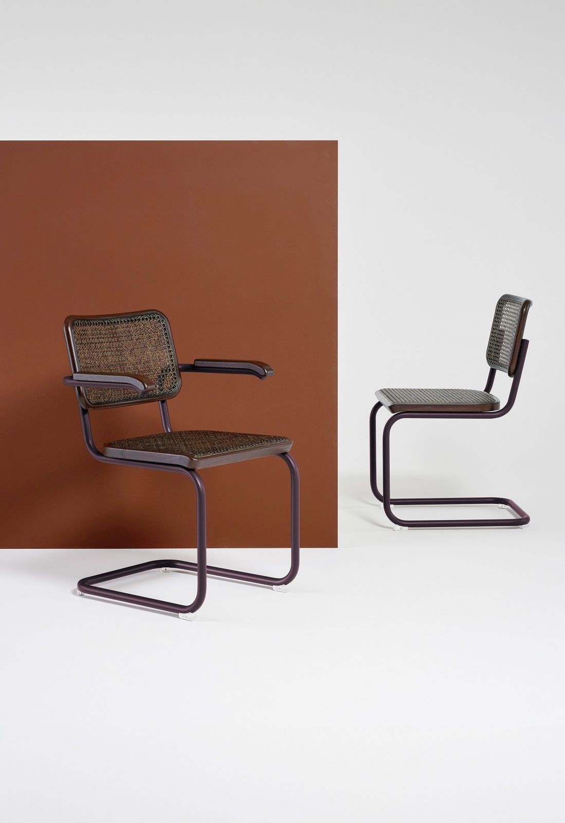 Zwei S 32 Freischwinger Stühle von Thonet mit Stahlrohrgestell und Wiener Geflecht vor braunem Hintergrund.
