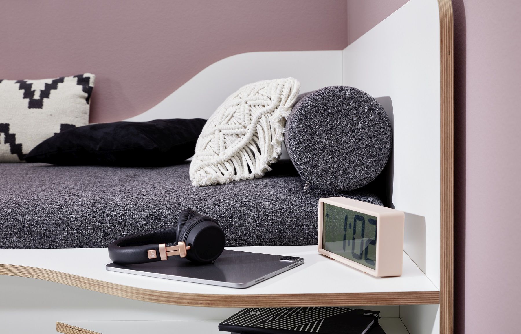 Detailaufnahme von Müllers Möbelwerkstätten Plane Einzelbett mit Kissen, Kopfhörern, Tablet und Uhr auf dem Nachttisch.