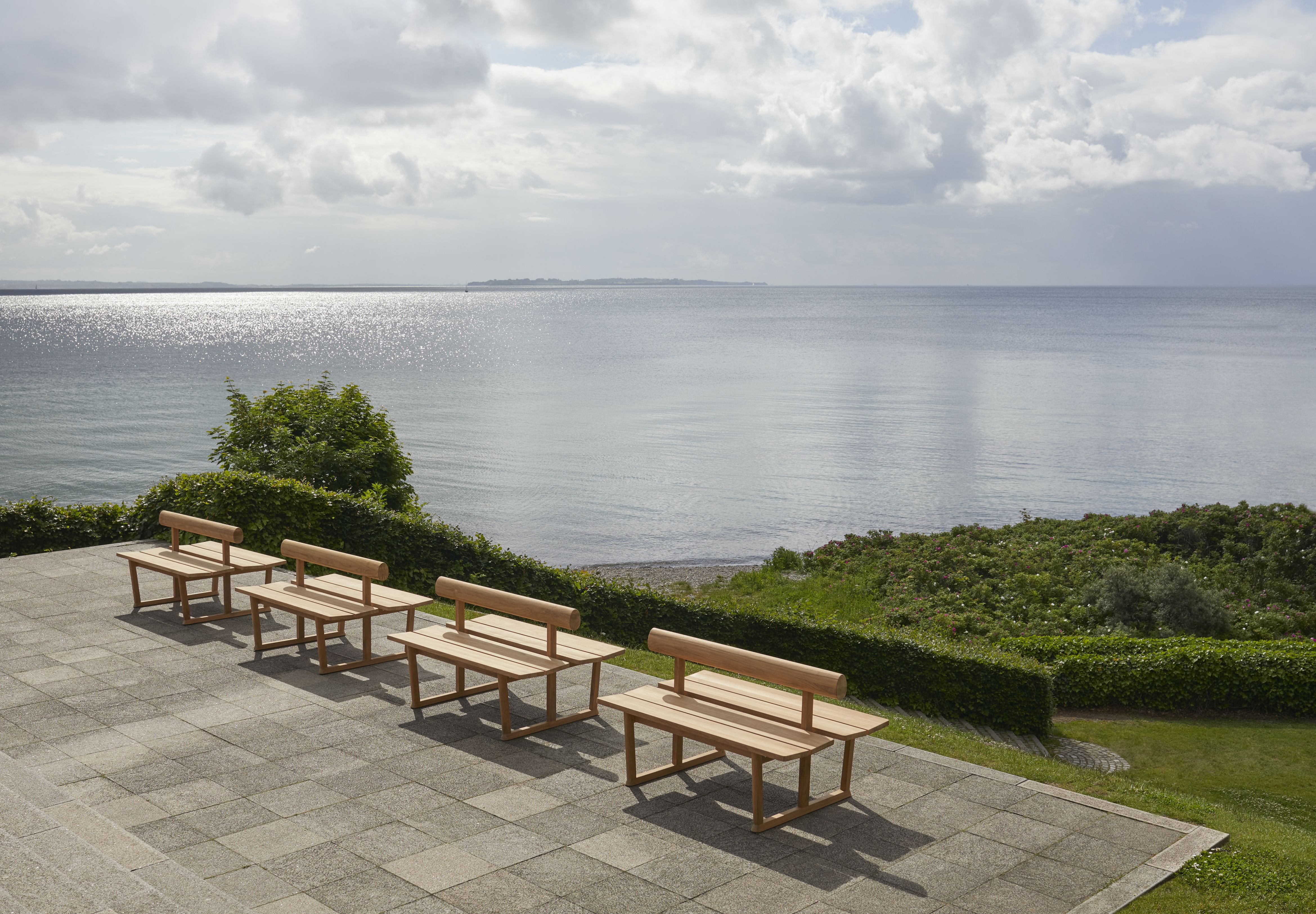 Reihe von Banco Teak Bänken von Skagerak im Außenbereich mit Meerblick. Gartenmöbel.