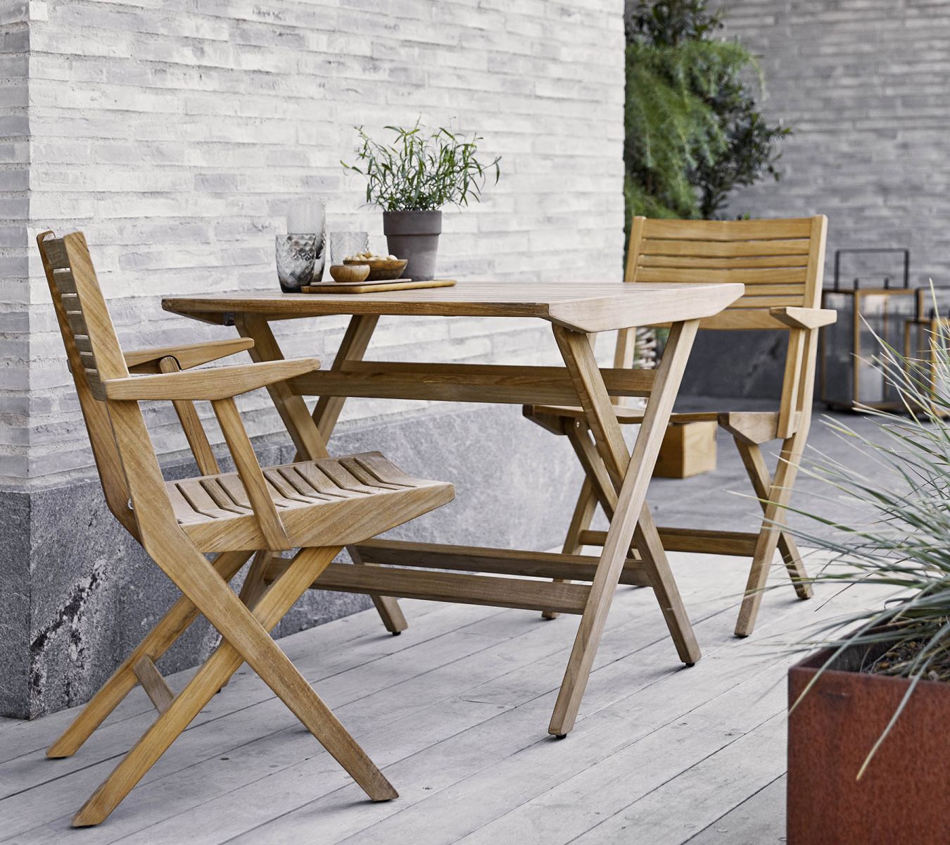 Cane-Line Flip Armlehnstuhl aus Teakholz mit passendem Gartentisch auf einer Terrasse, ideal für den Außenbereich.