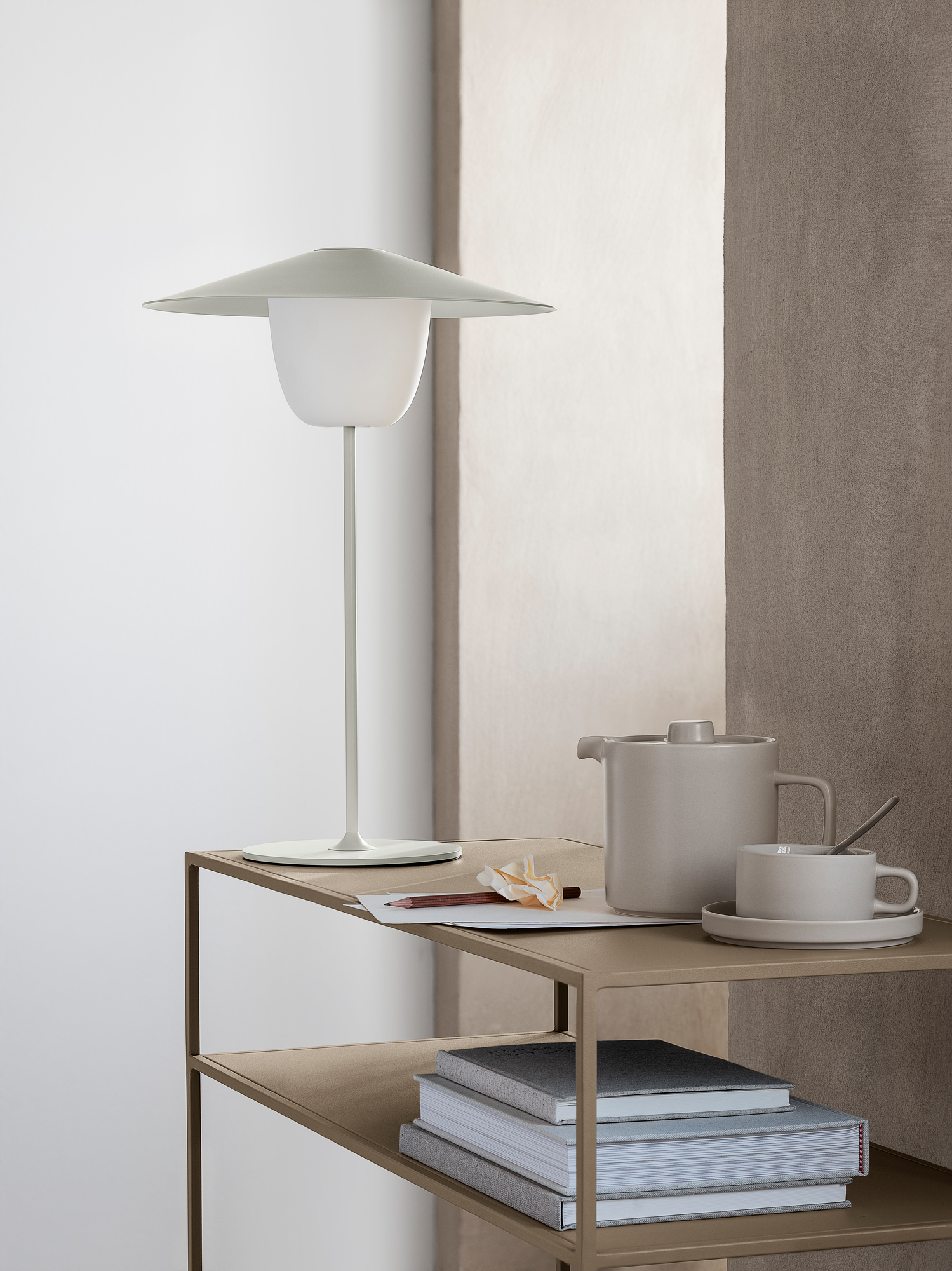 Ani Mobile LED Tischleuchte von Blomus auf Regal mit Teekanne und Tasse. Akkuleuchte für Innen.