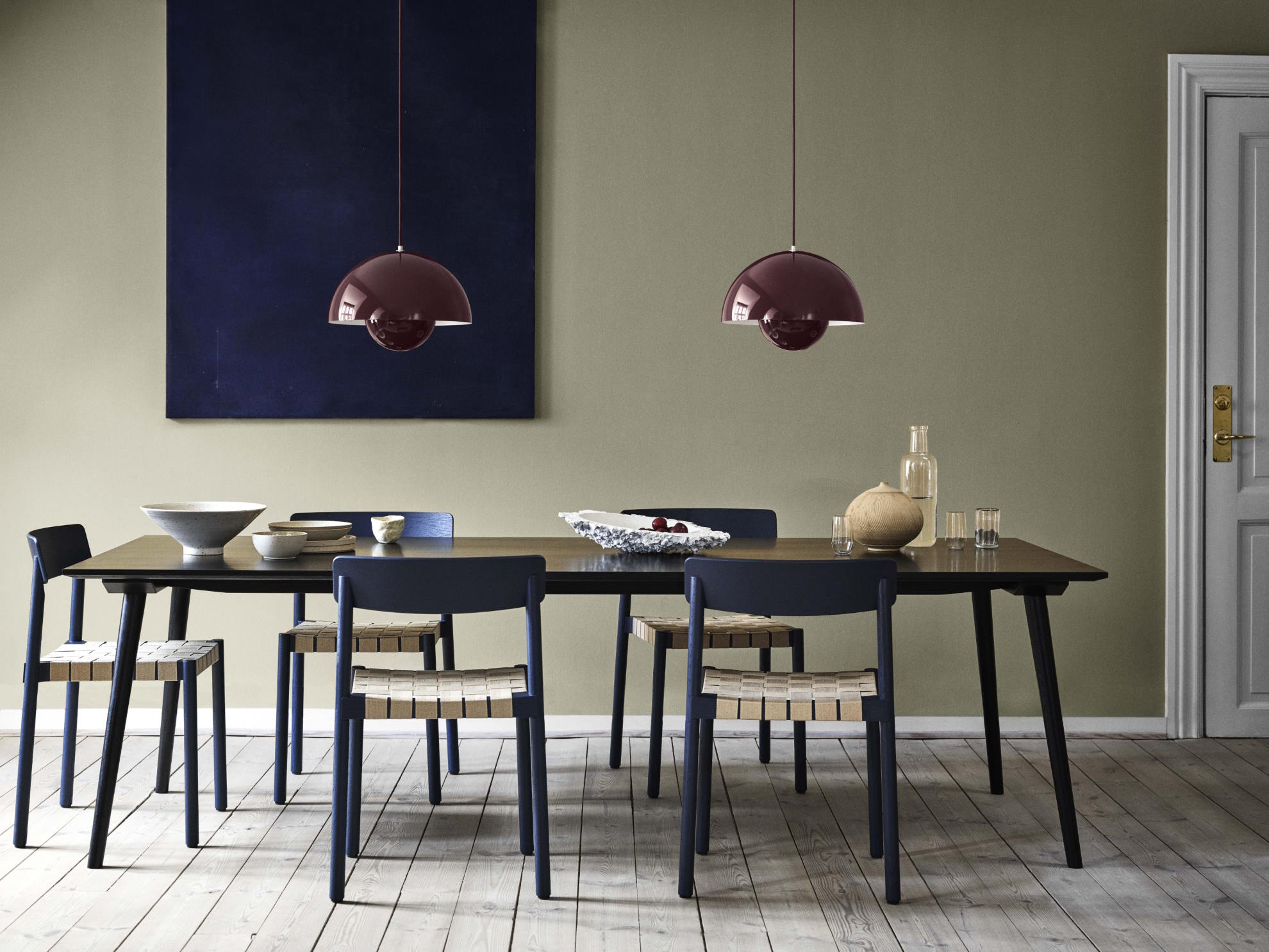 Esszimmer mit dunklem Holztisch, blauen Stühlen mit Webmuster und zwei burgunderroten Pendelleuchten.