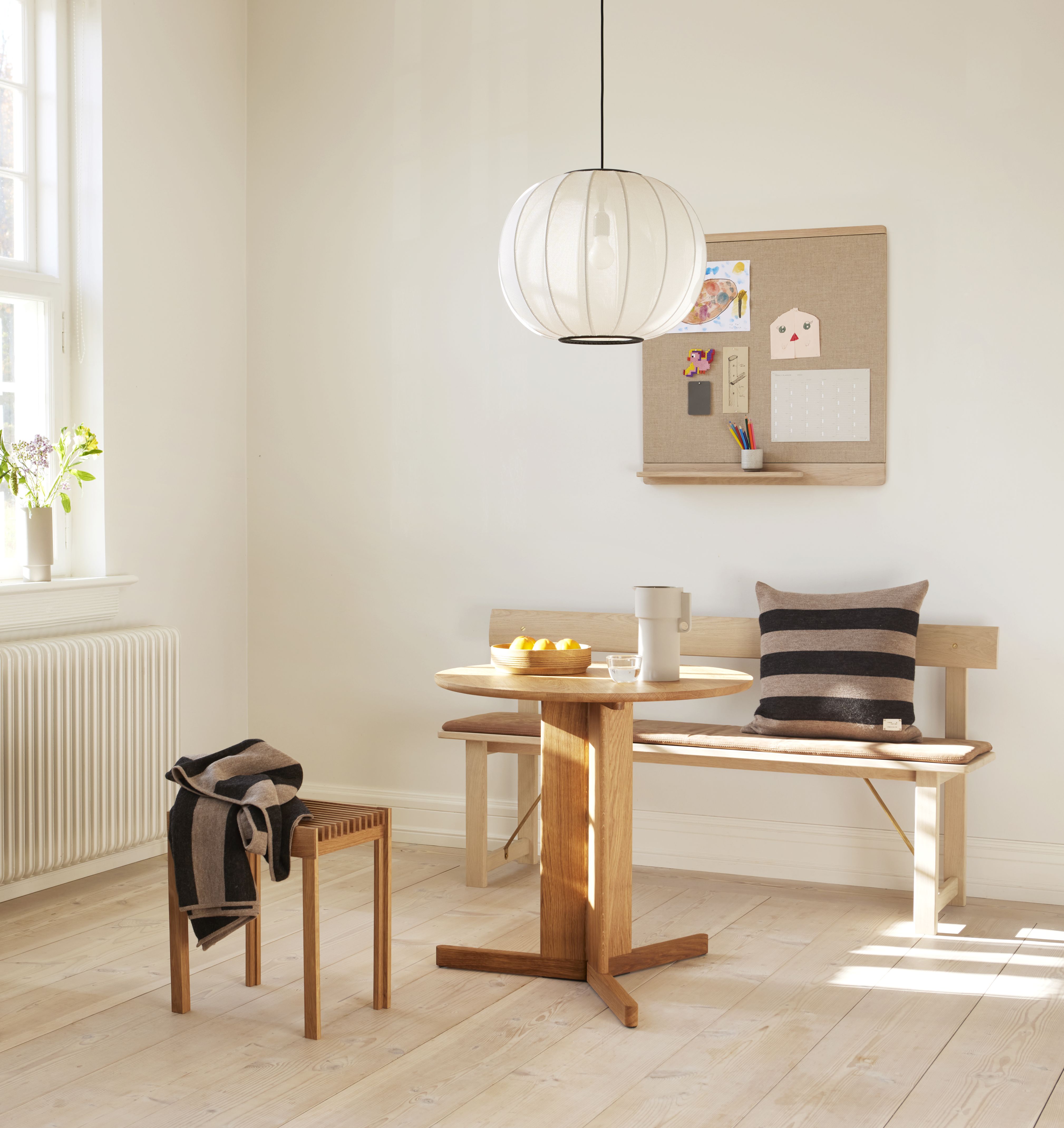 Helle Wohnraum-Szene mit Aymara Decke auf Hocker, gemütliche Textilien und Holztisch mit Bank.